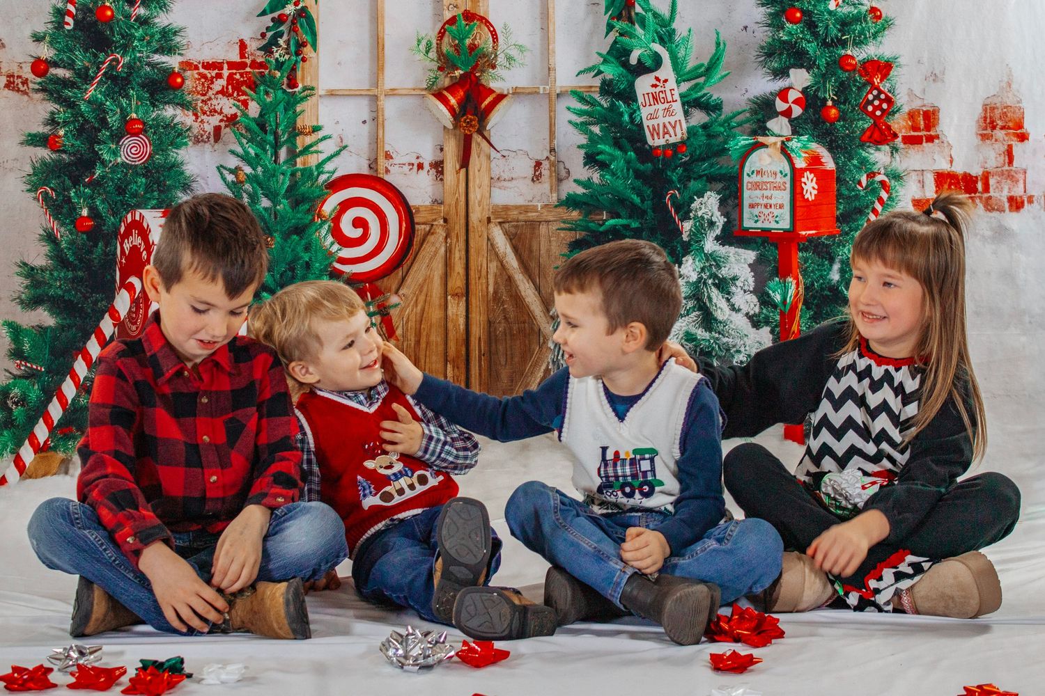 Four children laugh and interact playfully while seated together in a colorful Christmas photo backdrop.