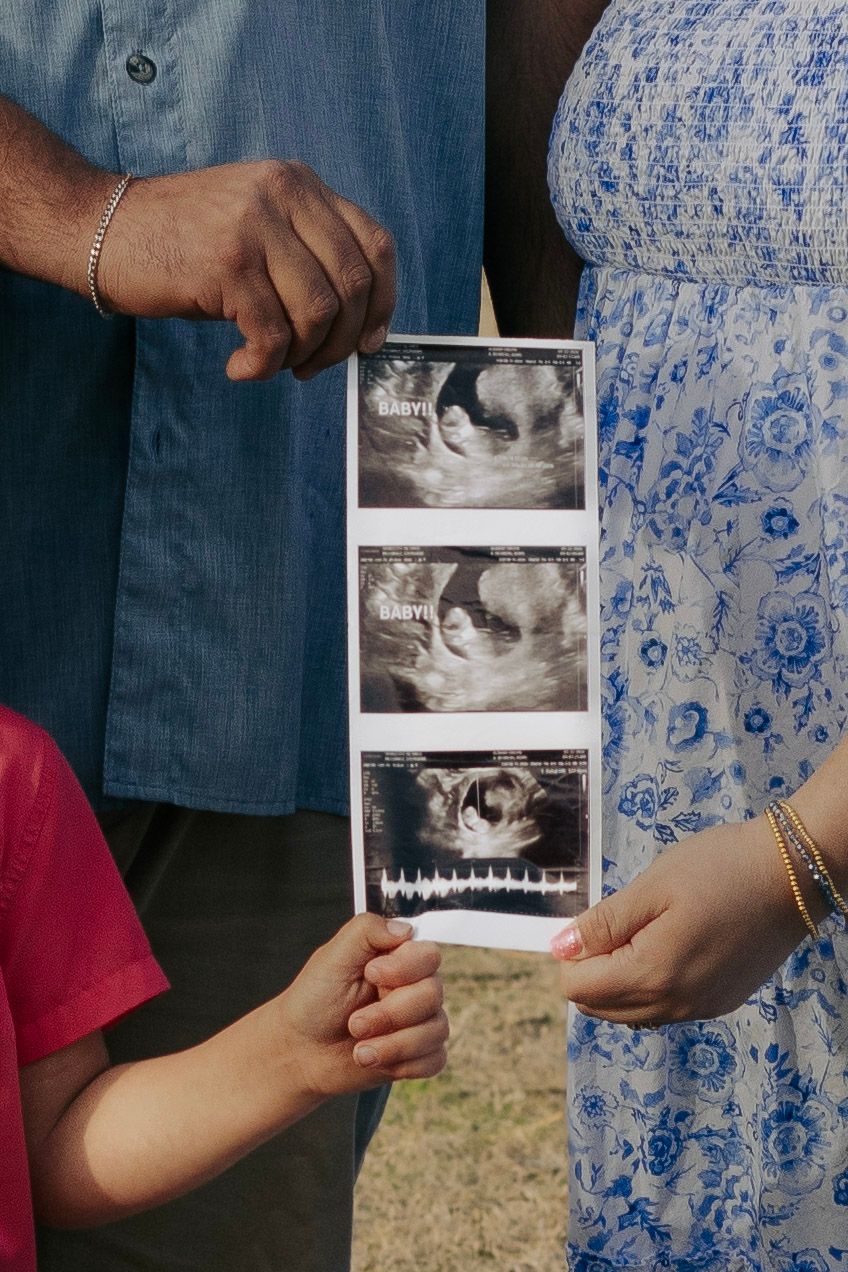 Family holding ultrasound strip outdoors for pregnancy announcement photo.