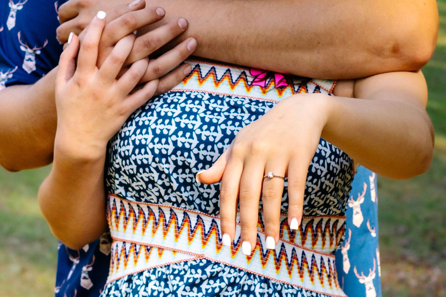 Close-up of couple embracing showing engagement ring, wearing colorful patterned outfits in outdoor setting.