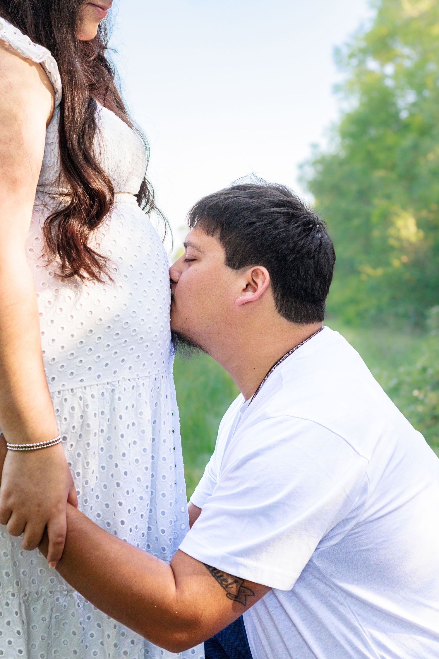 Man kissing pregnant woman's belly outdoors, couple sharing tender maternity moment in nature.