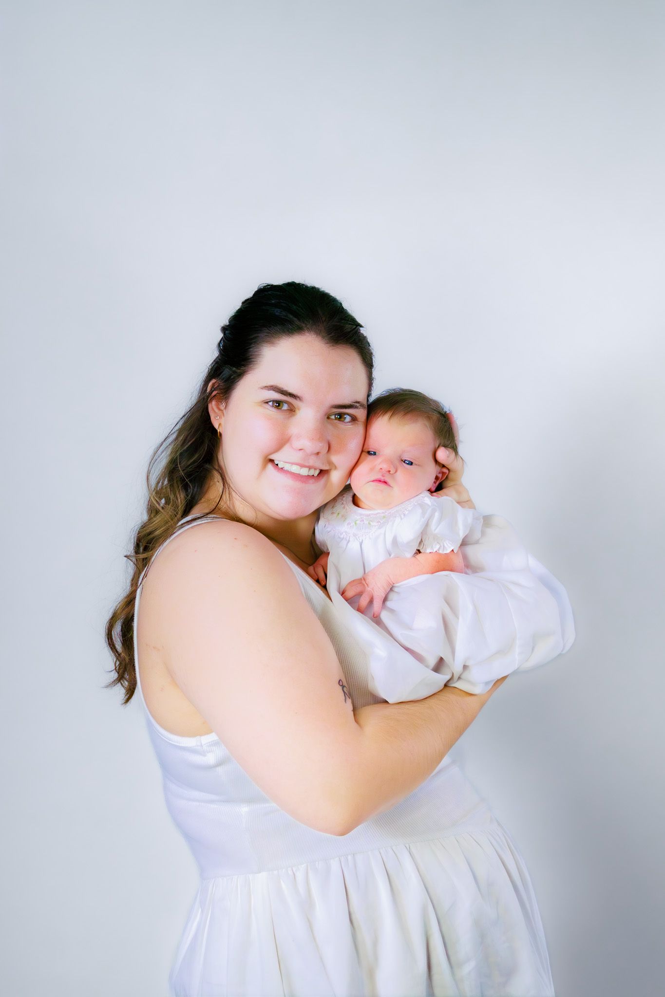 Smiling mother in white dress holding her newborn baby against white background.