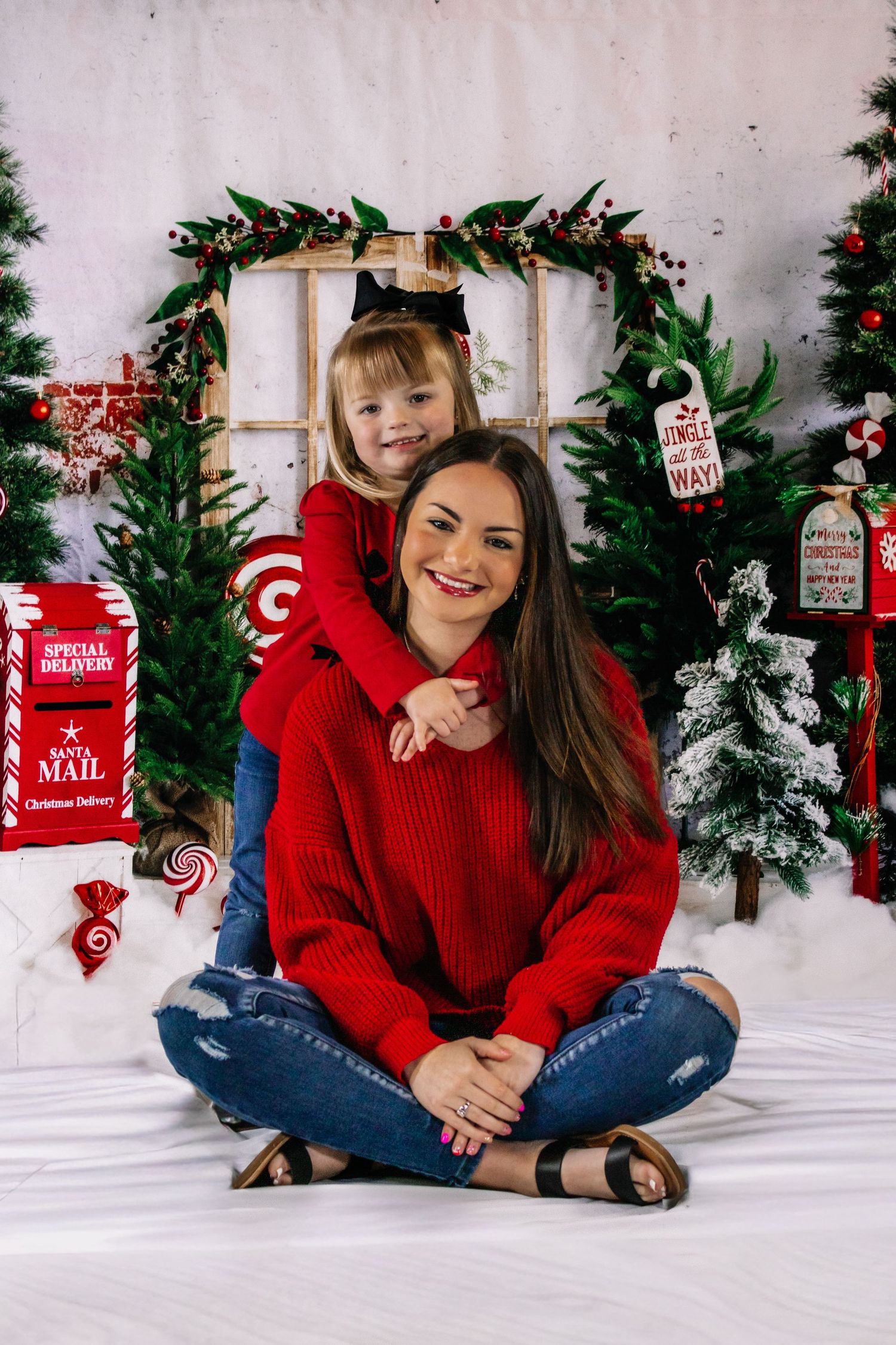 Mother and young daughter in matching red outfits posing in festive Christmas photo studio.