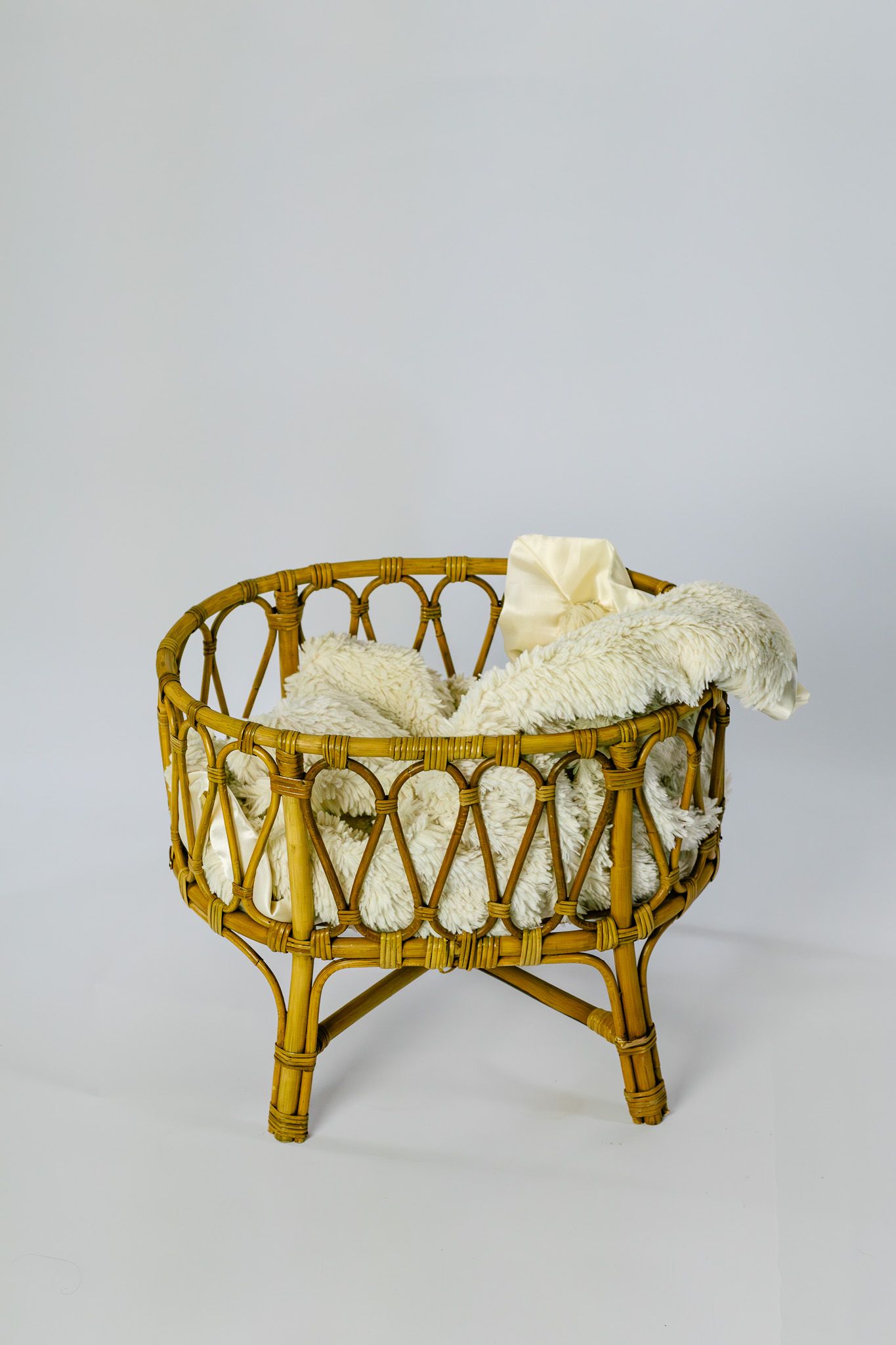 Vintage wicker rattan baby bassinet with white fluffy blanket on gray background.