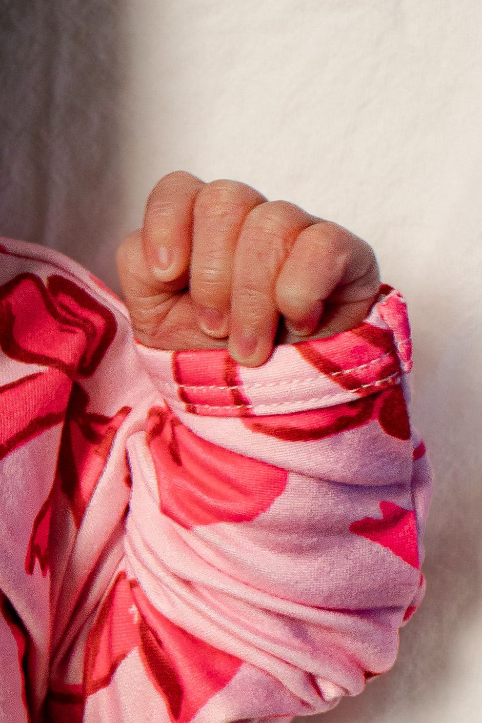 Close-up of tiny newborn baby fist in pink floral onesie sleeve.