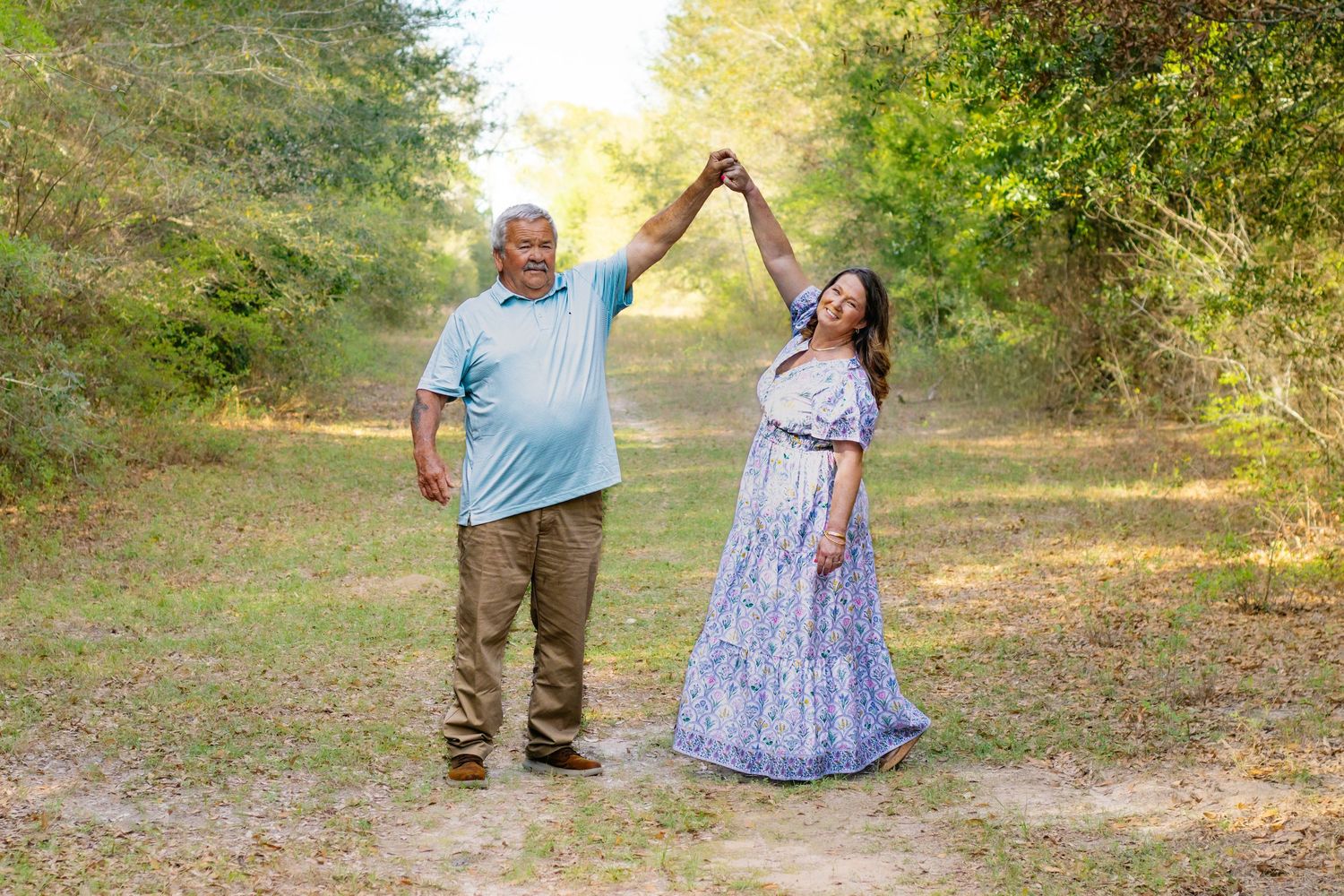 Couple dancing outdoors on a dirt path surrounded by lush green trees in summer.