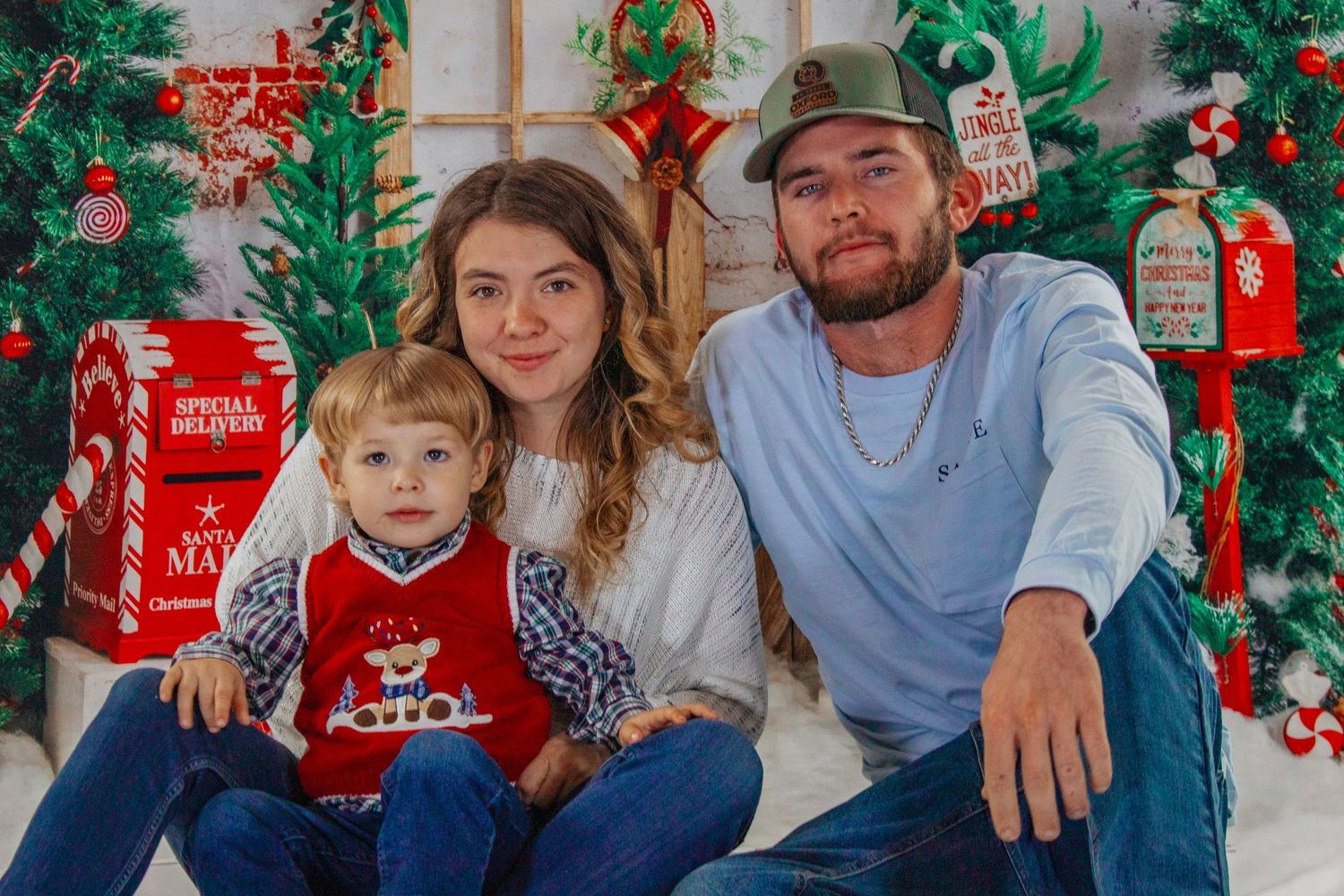 Young family with toddler posing for Christmas portrait with festive holiday backdrop and decorations.