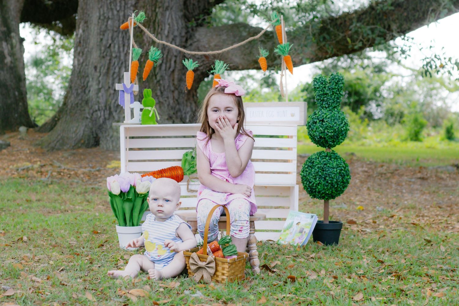 Girl in pink outfit and baby sit together at Easter photo set with spring decorations.