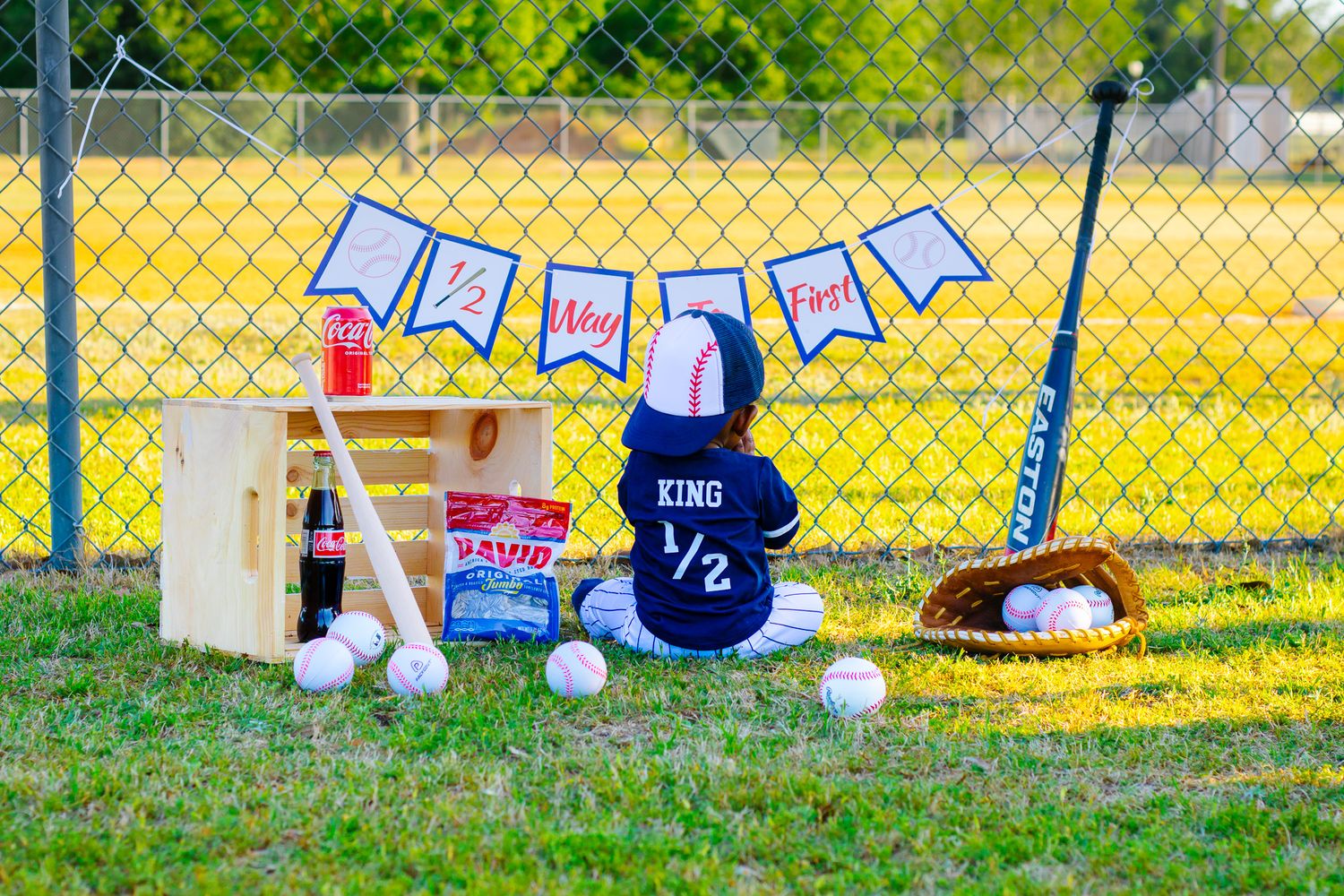 Baby's baseball-themed half birthday setup with stuffed bunny in KING jersey, baseballs, bat, and decorative banner outdoors.