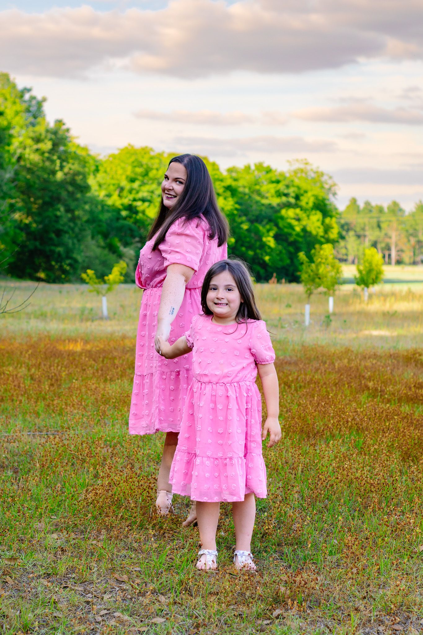 Mother and daughter in matching pink dresses smiling together in a green field.