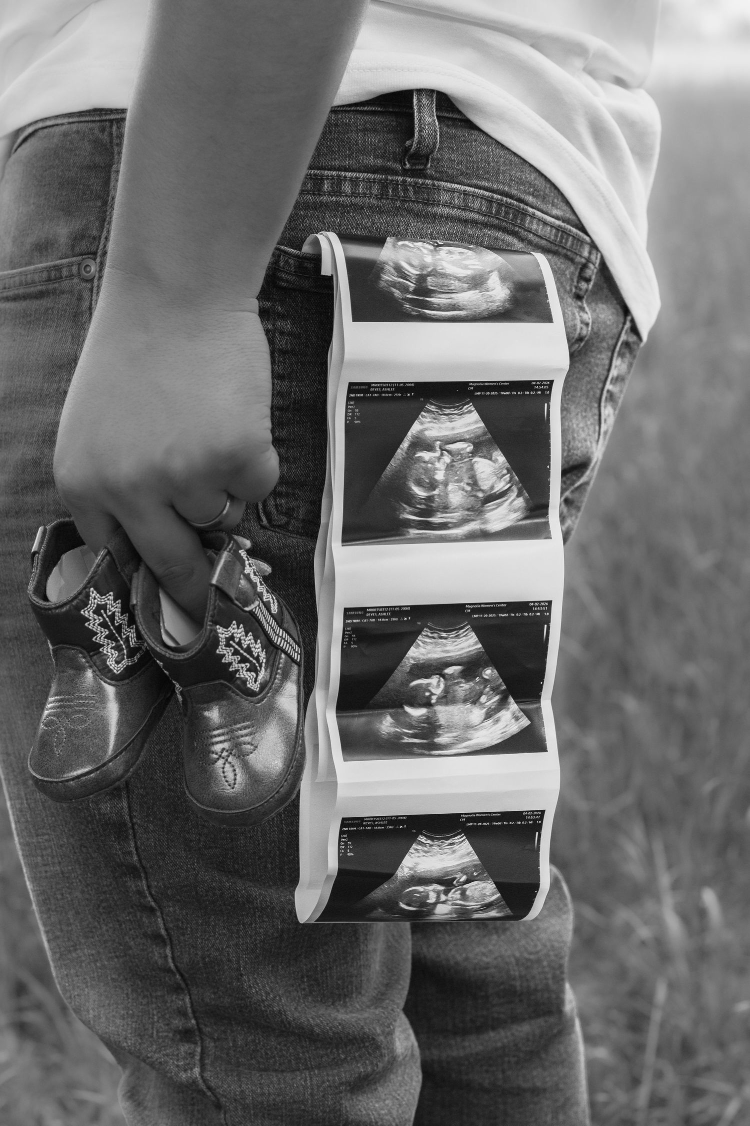 Black and white photo of pregnant woman holding baby shoes and ultrasound strip, pregnancy announcement concept.