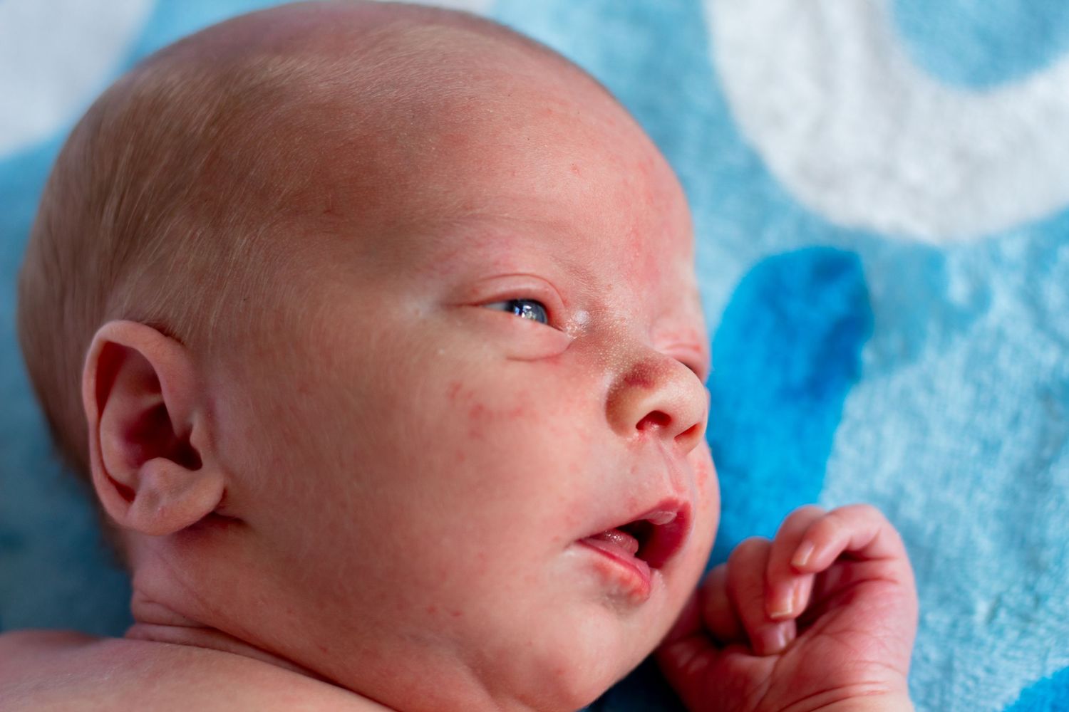 Close-up portrait of a newborn baby lying on a blue blanket, eyes open.