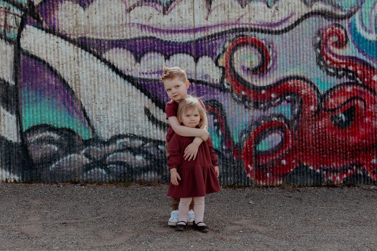 A person in a red dress poses in front of a colorful graffiti wall with swirling purple and blue designs.