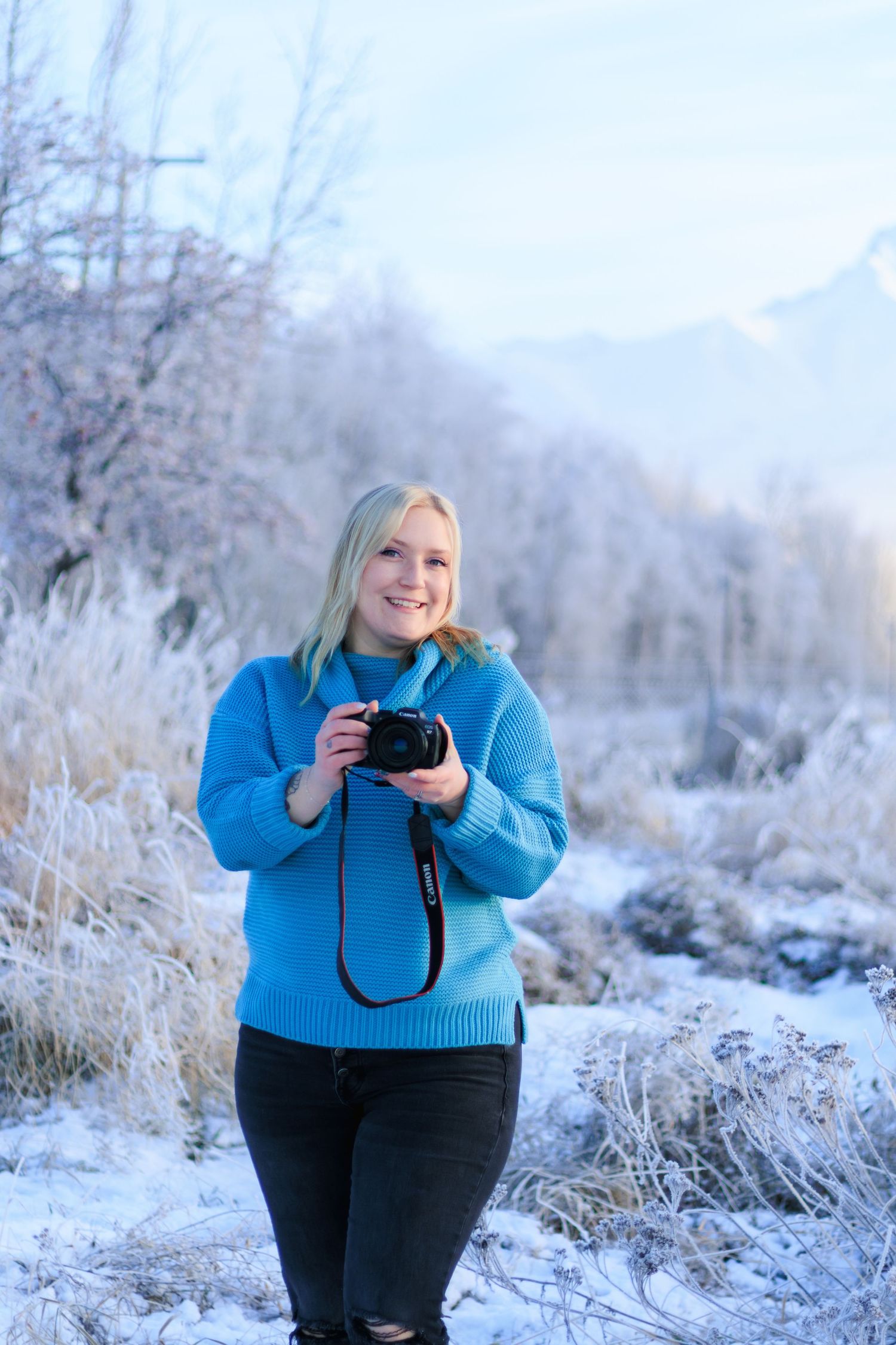 A photographer wearing a bright blue sweater captures winter scenes in a frosty, snow-covered landscape.