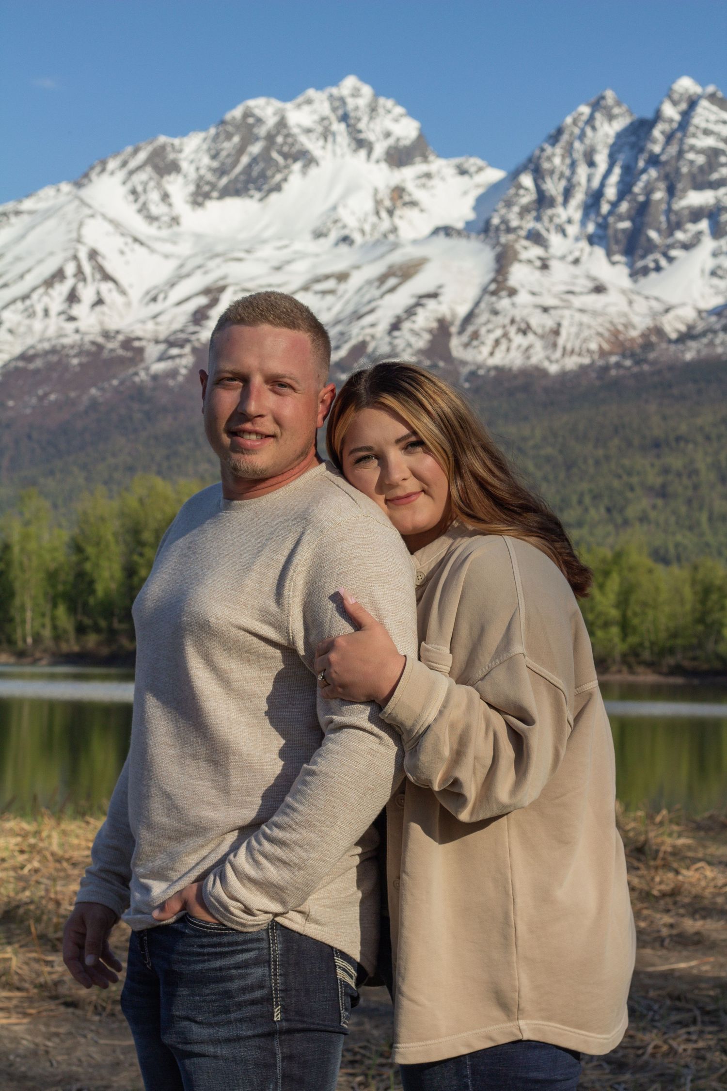 A couple poses together in front of a scenic mountain lake landscape on a clear day.