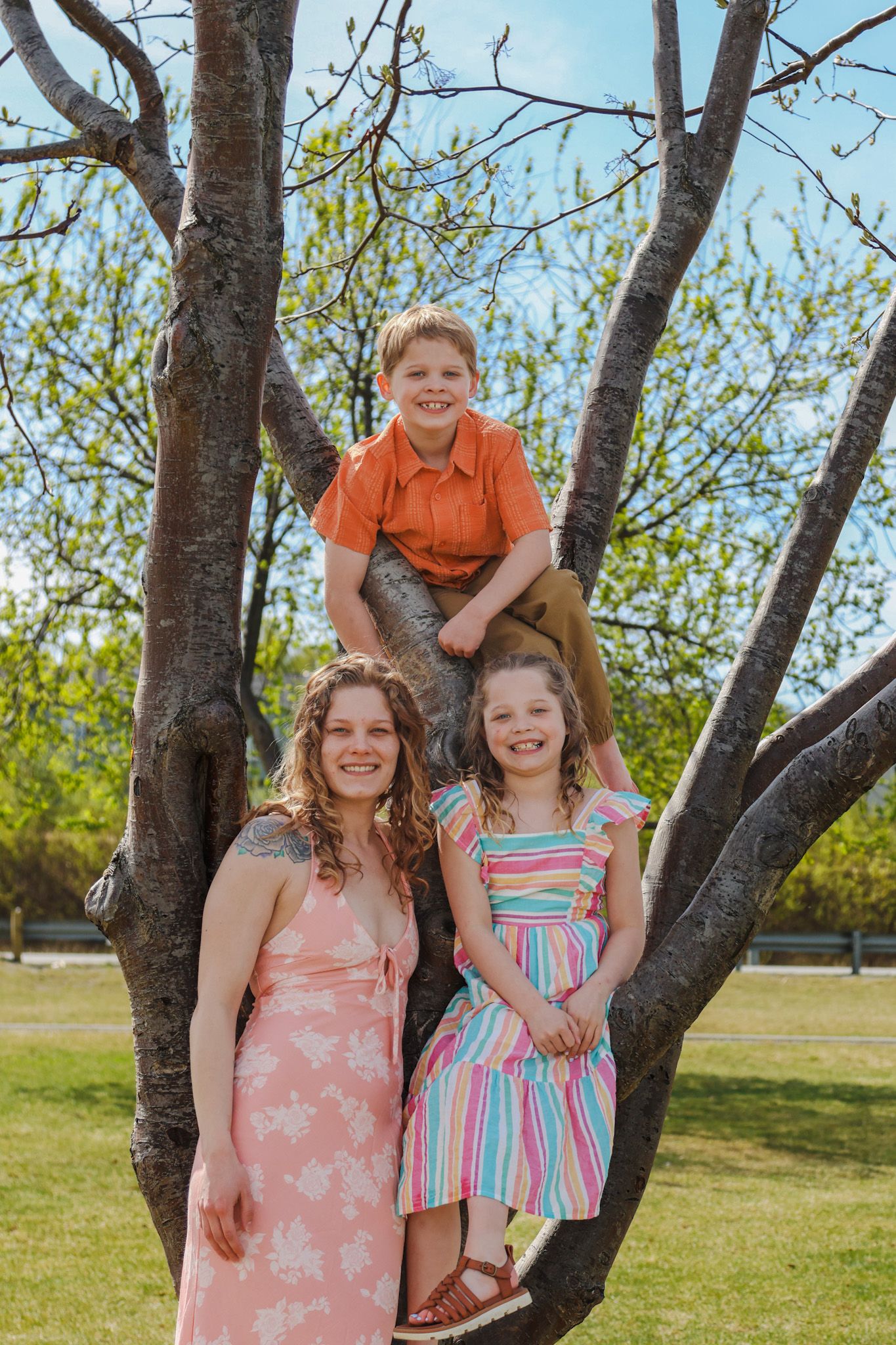 A family poses together in front of a blooming spring tree in a grassy field on a sunny day.