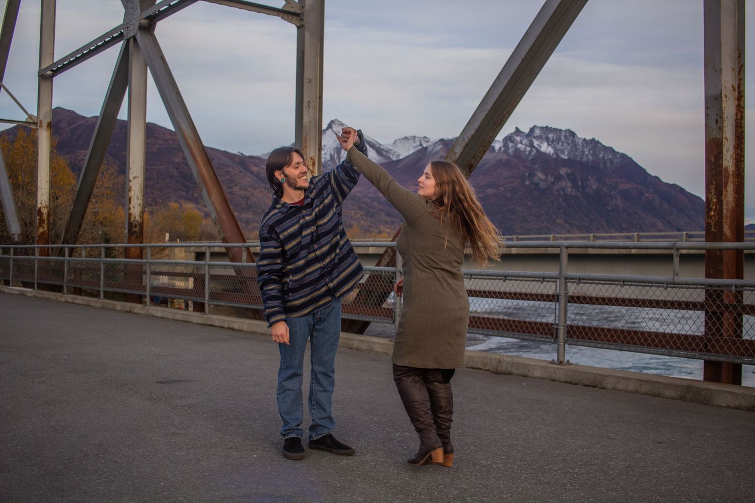 Two people walking together on a wooden boardwalk with mountains visible in the background on a cloudy day.