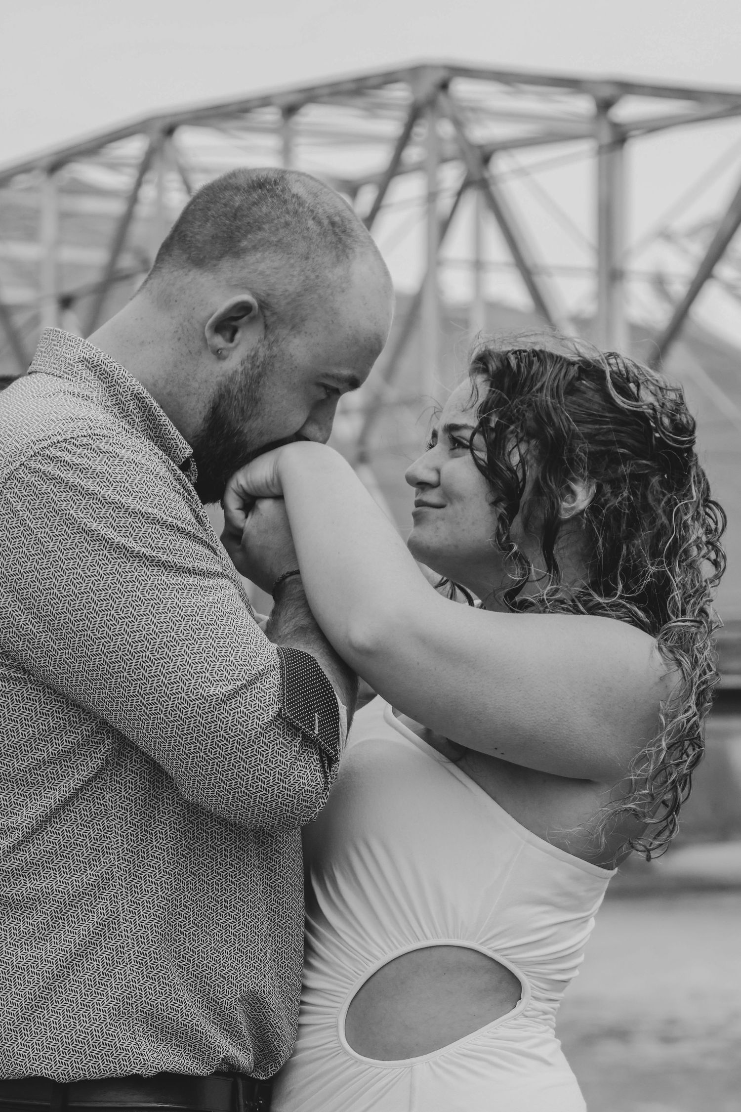 A romantic black and white photo series of a couple embracing and kissing on a bridge.