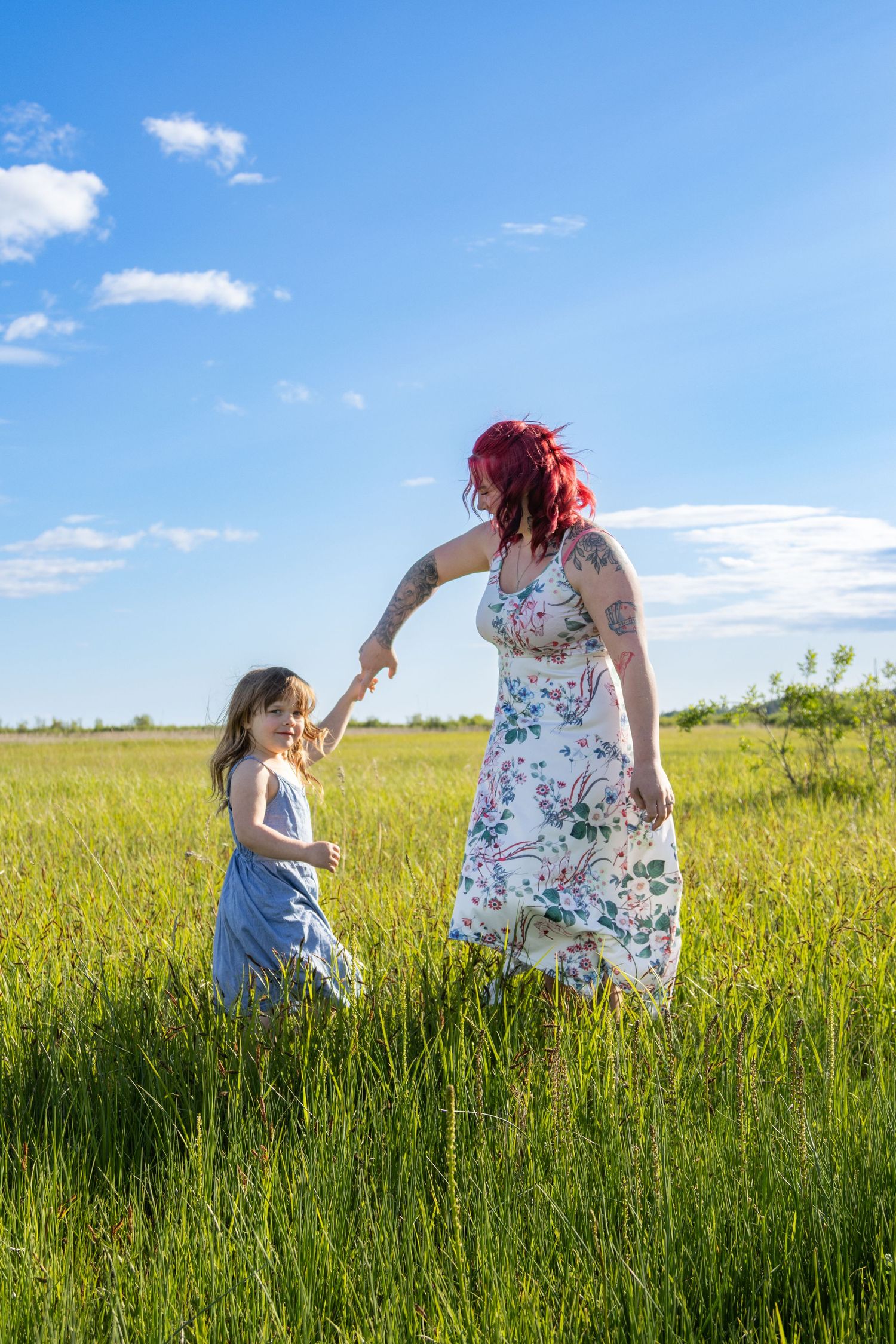Two people in a sunny meadow with tall grass and wildflowers under bright blue summer skies.
