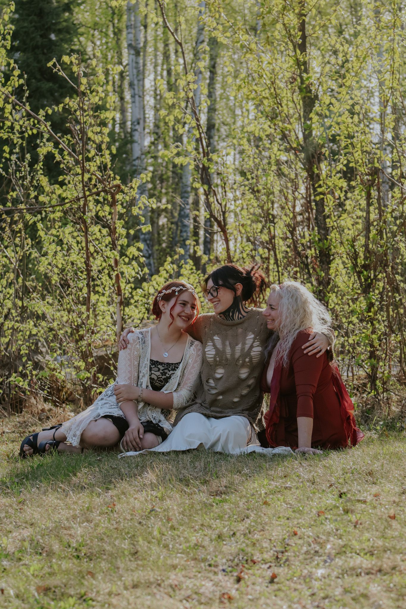 A group relaxes together on grassy ground surrounded by sunlit birch trees in an autumn forest setting.
