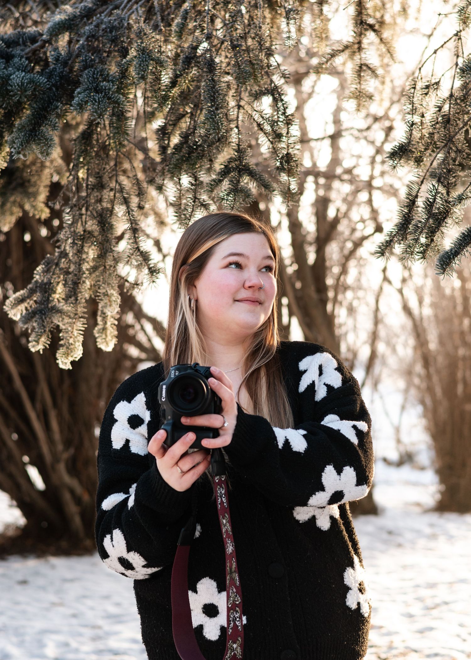 A person in a black sweater with white floral designs poses playfully in a snowy winter forest setting.