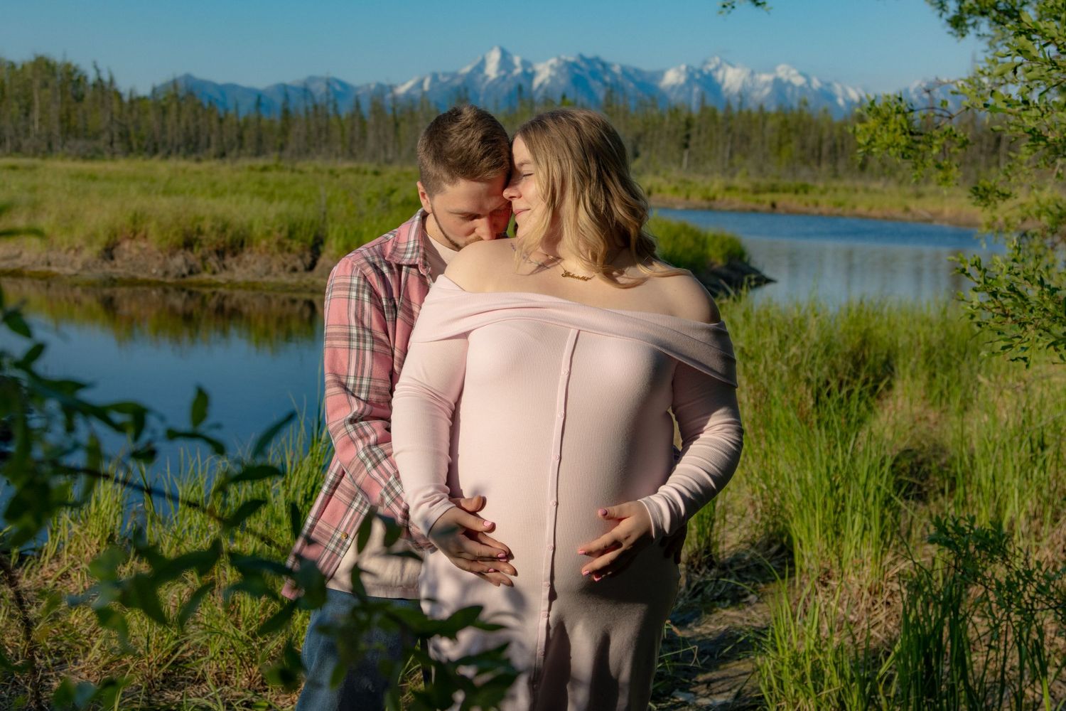 Couple embraces while enjoying scenic mountain views in a grassy meadow during golden hour.