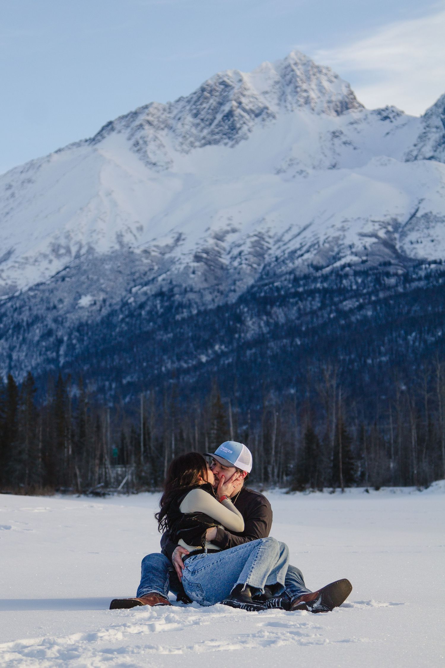 Photographer lying in snowy landscape capturing shots with mountains in background during winter.