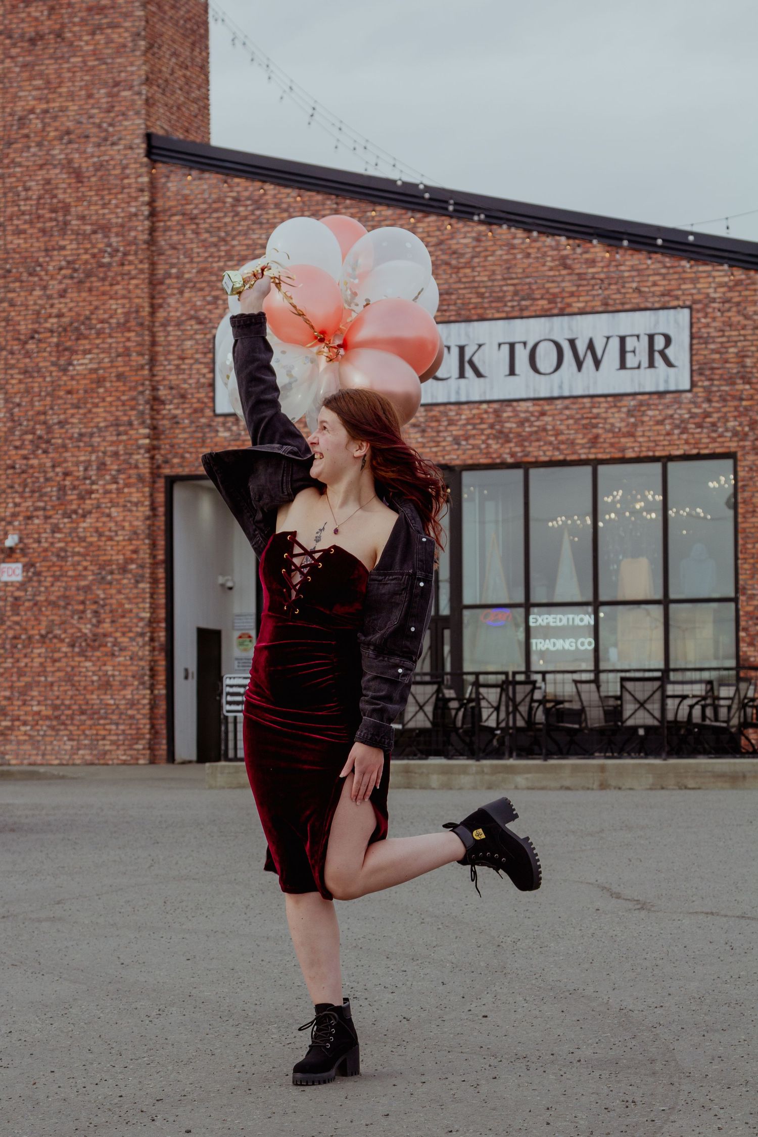 A person in a black dress and large pink floral headpiece poses against a brick building exterior.