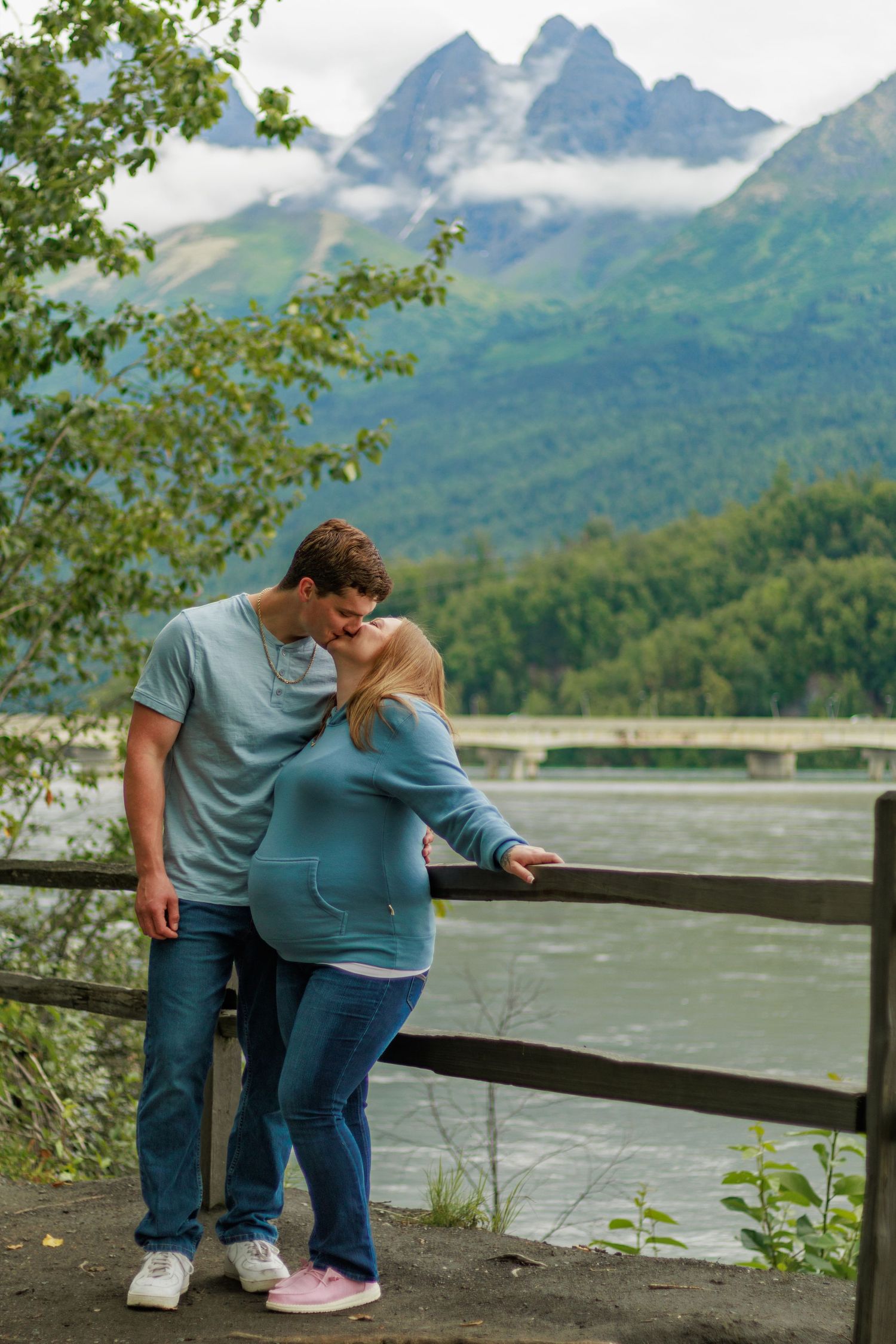 A couple shares an intimate moment overlooking a scenic mountain lake with misty peaks in the background.