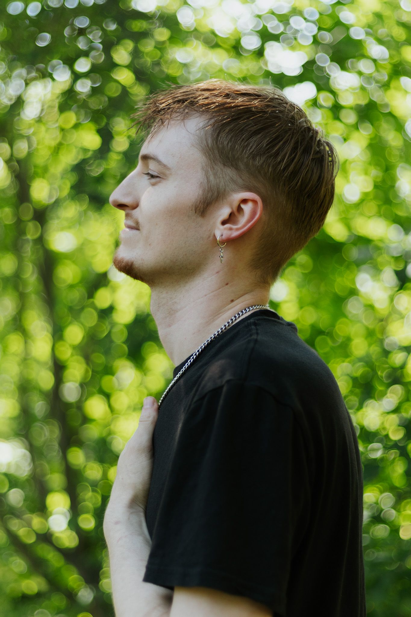 Profile silhouette of person in black shirt against blurred green foliage background in natural lighting.