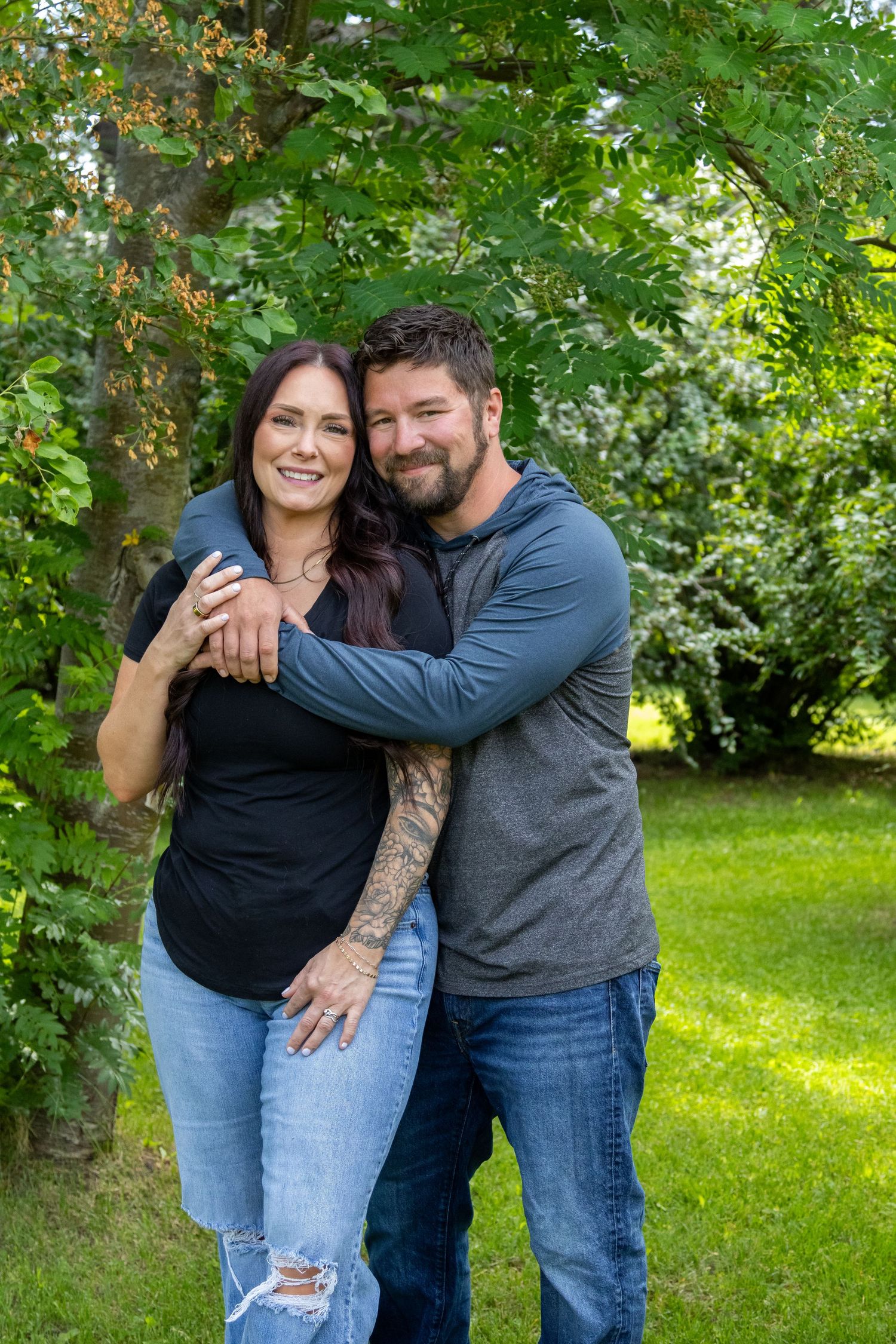 A couple embraces outdoors in a lush green garden setting while sharing affectionate moments together.