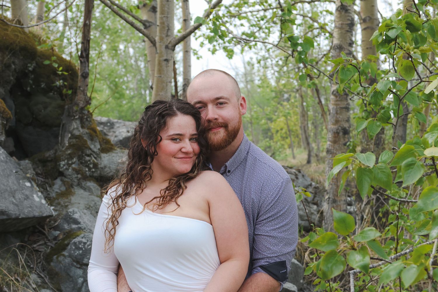 A couple shares tender moments together in a lush green forest setting during their outdoor photo session.