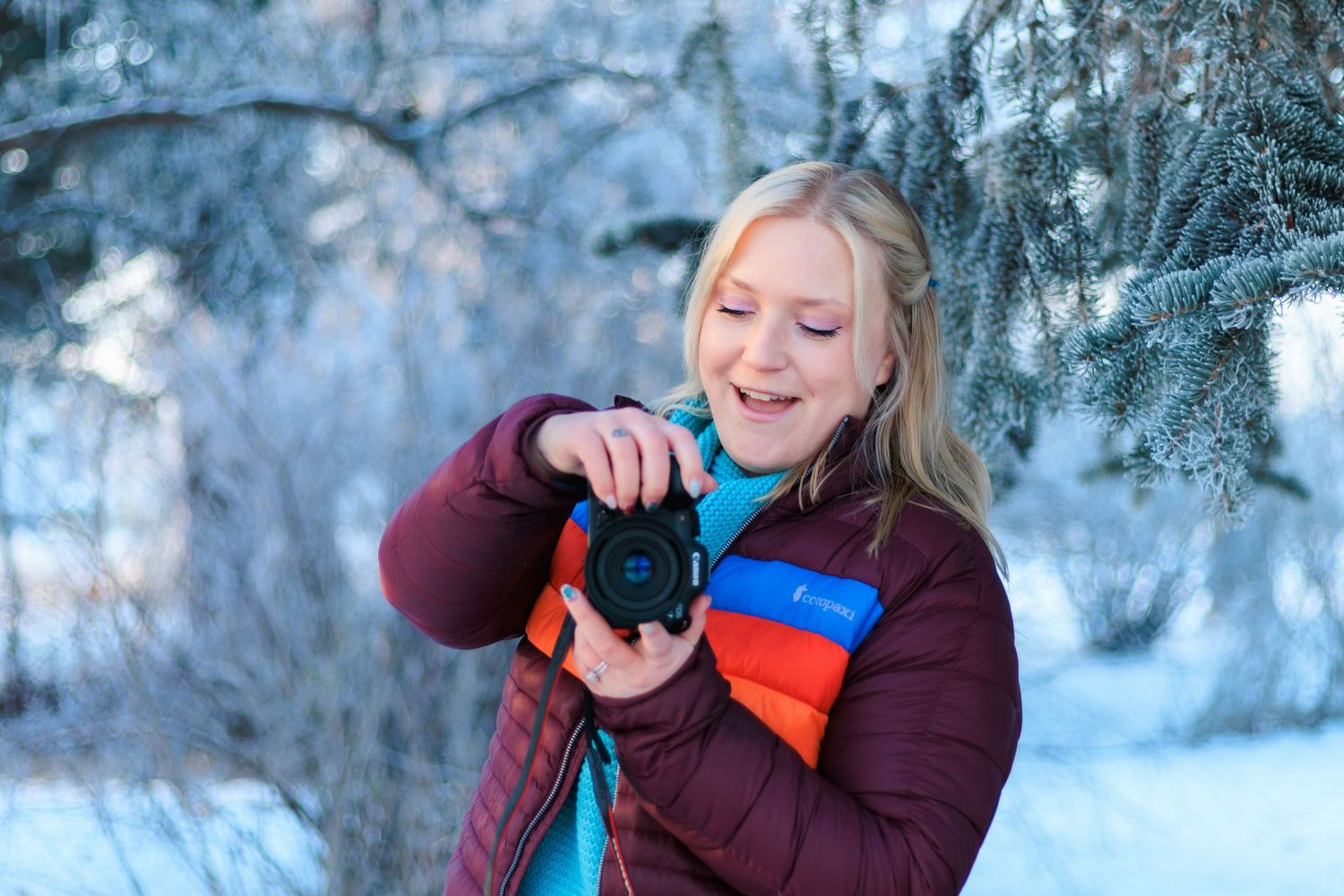 A photographer in a burgundy coat captures winter scenes in a snowy landscape with a professional camera.