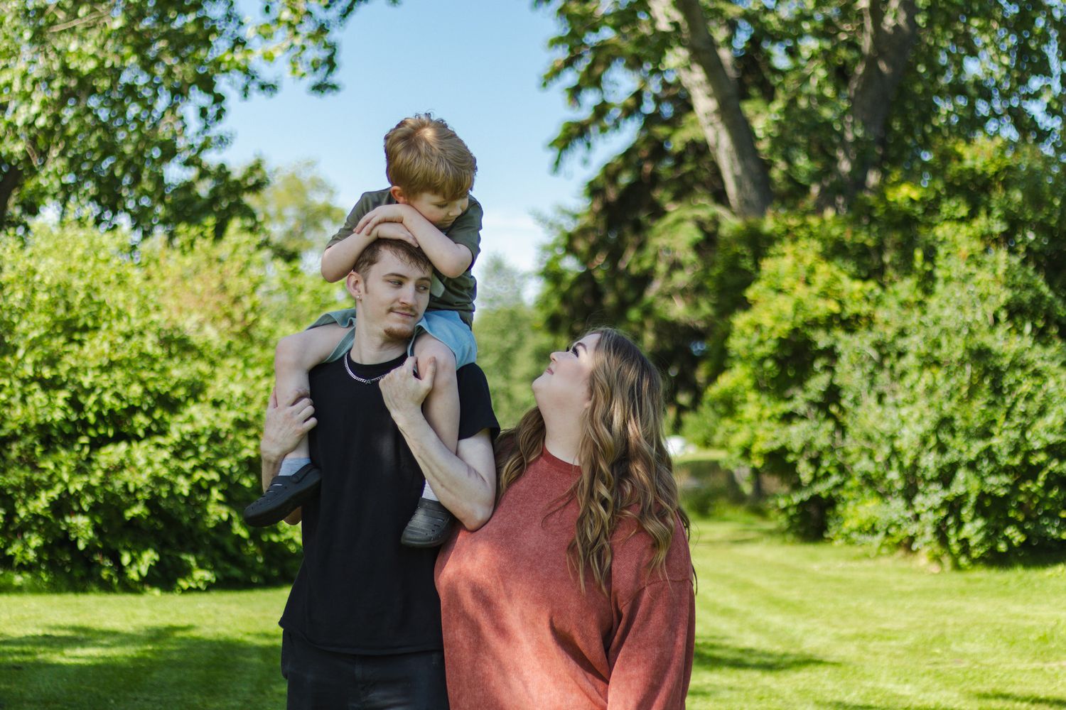 A couple shares romantic moments in a lush green garden setting during a summer photoshoot.