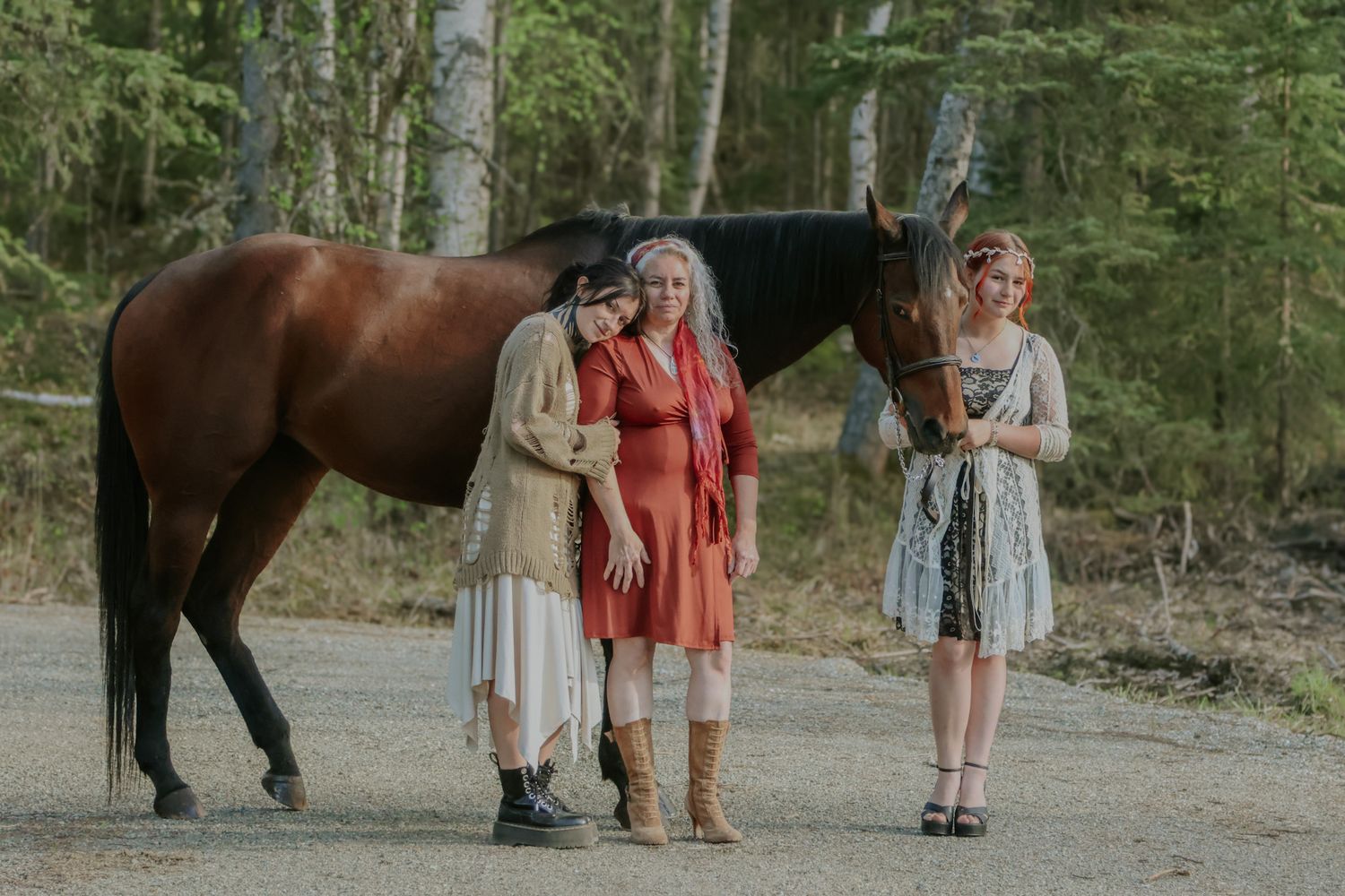 A horse walking along a wooded trail with people in summer dresses and casual attire.