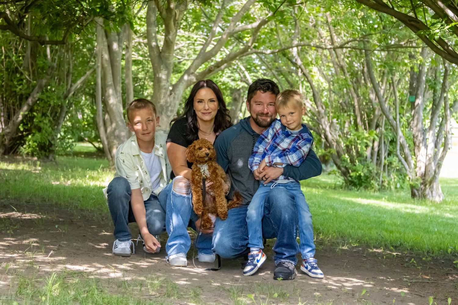 People sitting together outdoors on blankets enjoying a sunny day in a wooded park setting.