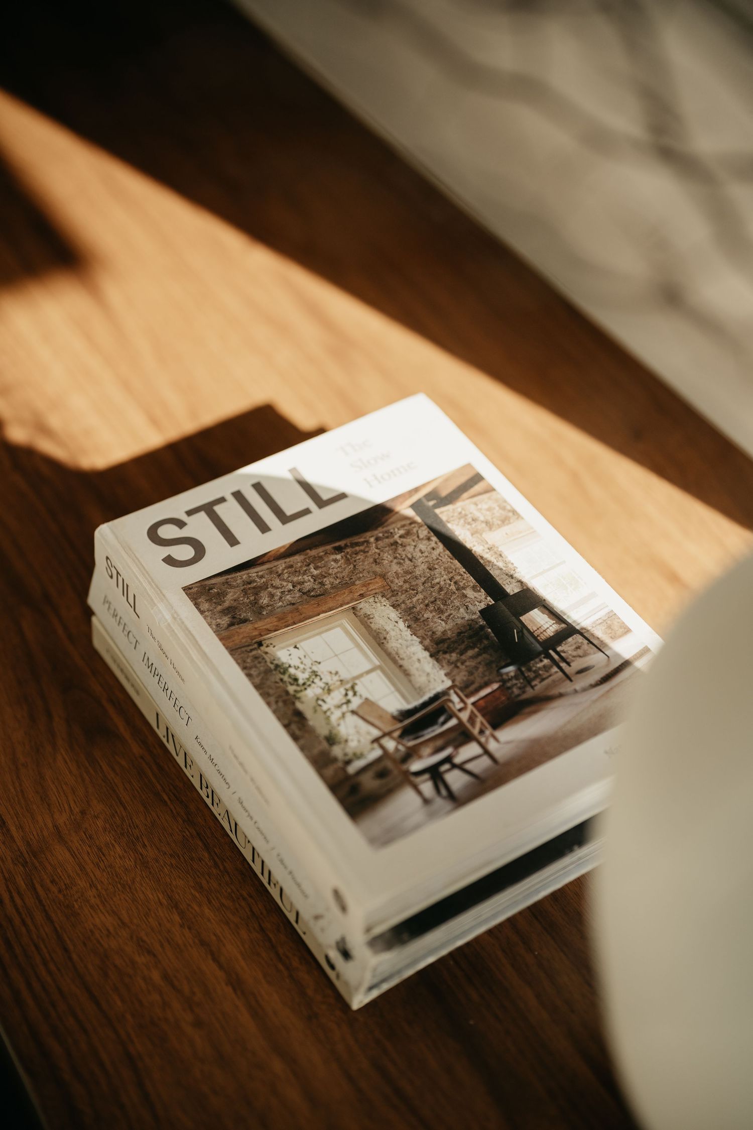 Stack of STILL interior design books on wooden table in warm sunlight.