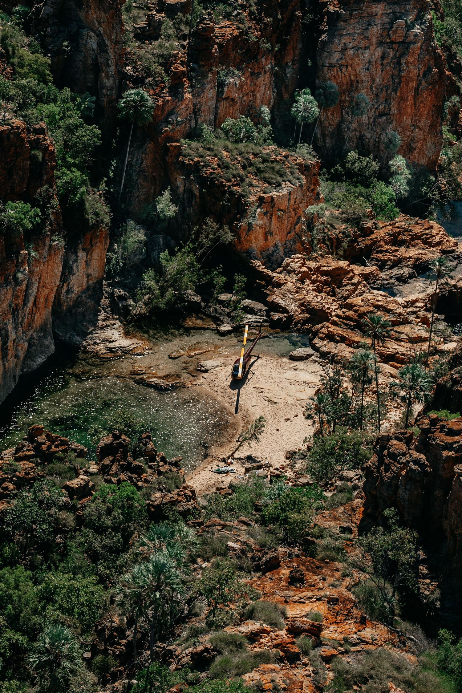 Aerial view of a rugged red rock canyon with lush green vegetation and sandy floor in Australia.