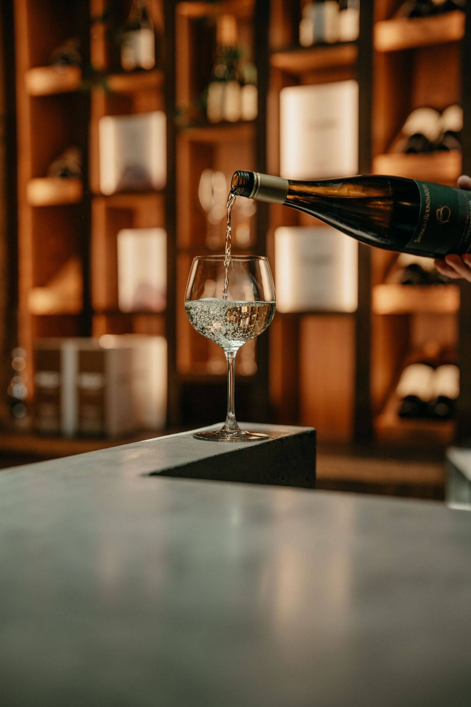 White wine being poured into a glass in a warmly lit wine cellar.
