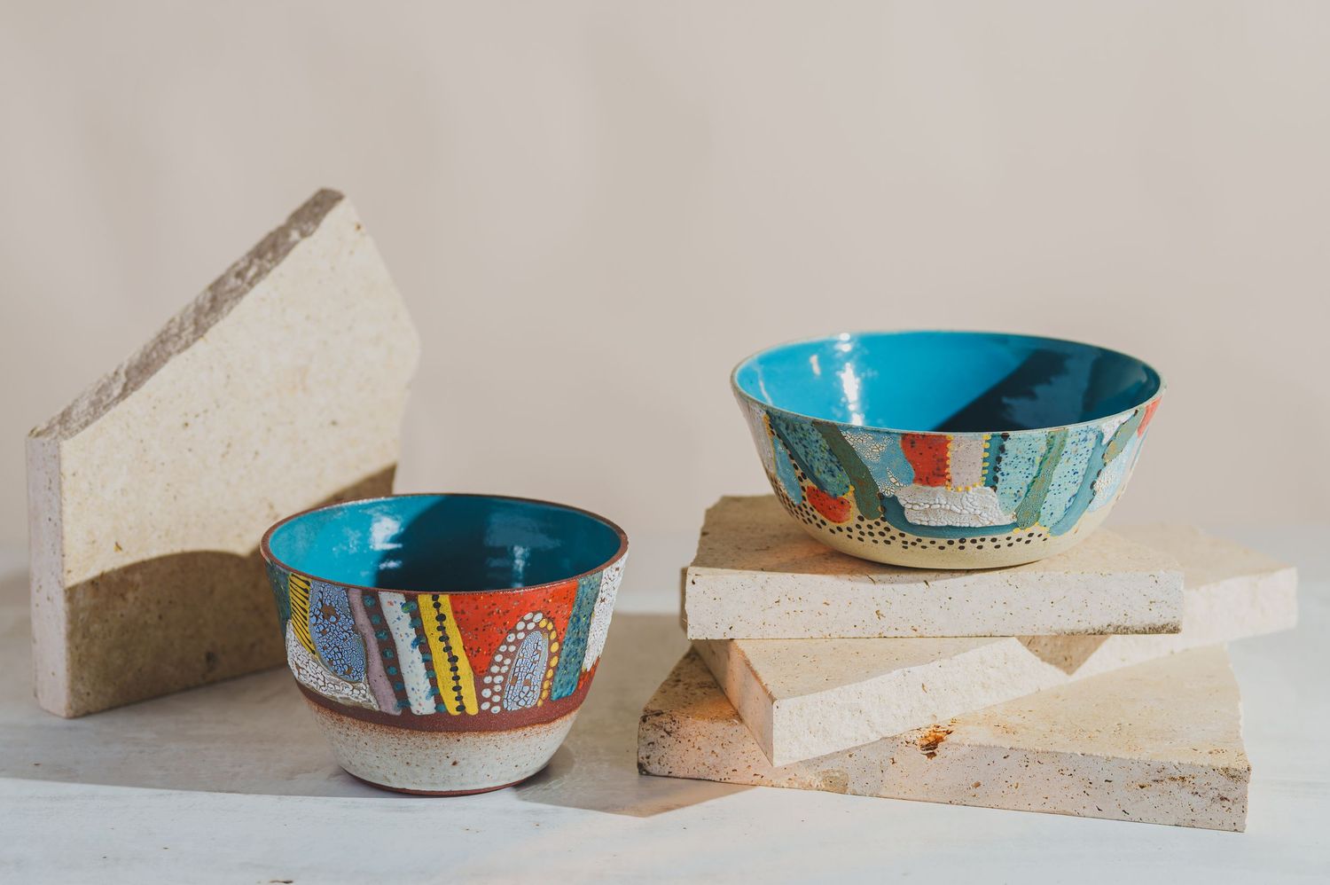 Two colorful hand-painted ceramic bowls with turquoise interiors displayed on rustic stone blocks.