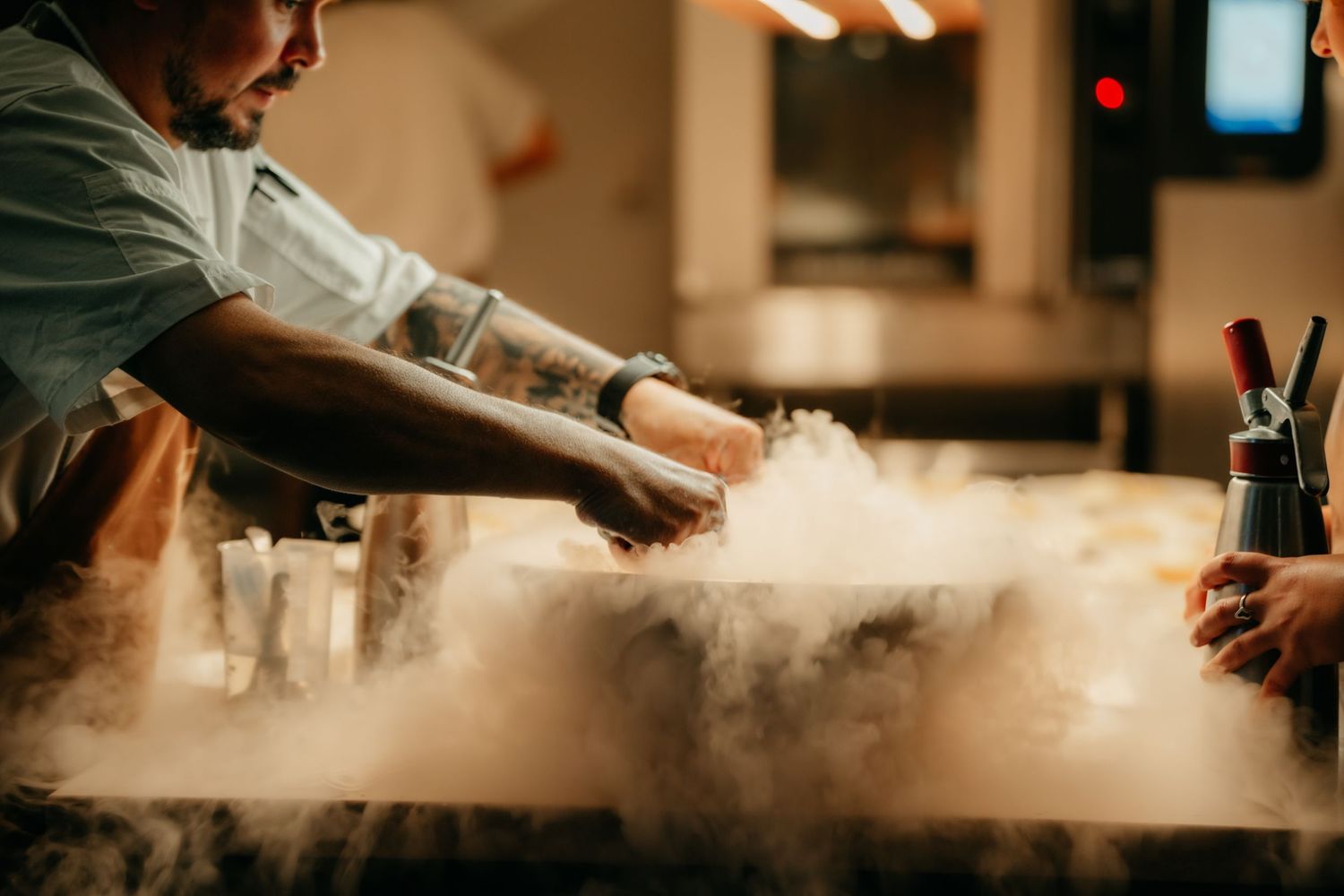 Chef using liquid nitrogen to create dramatic smoke effects on a dish in a restaurant kitchen.