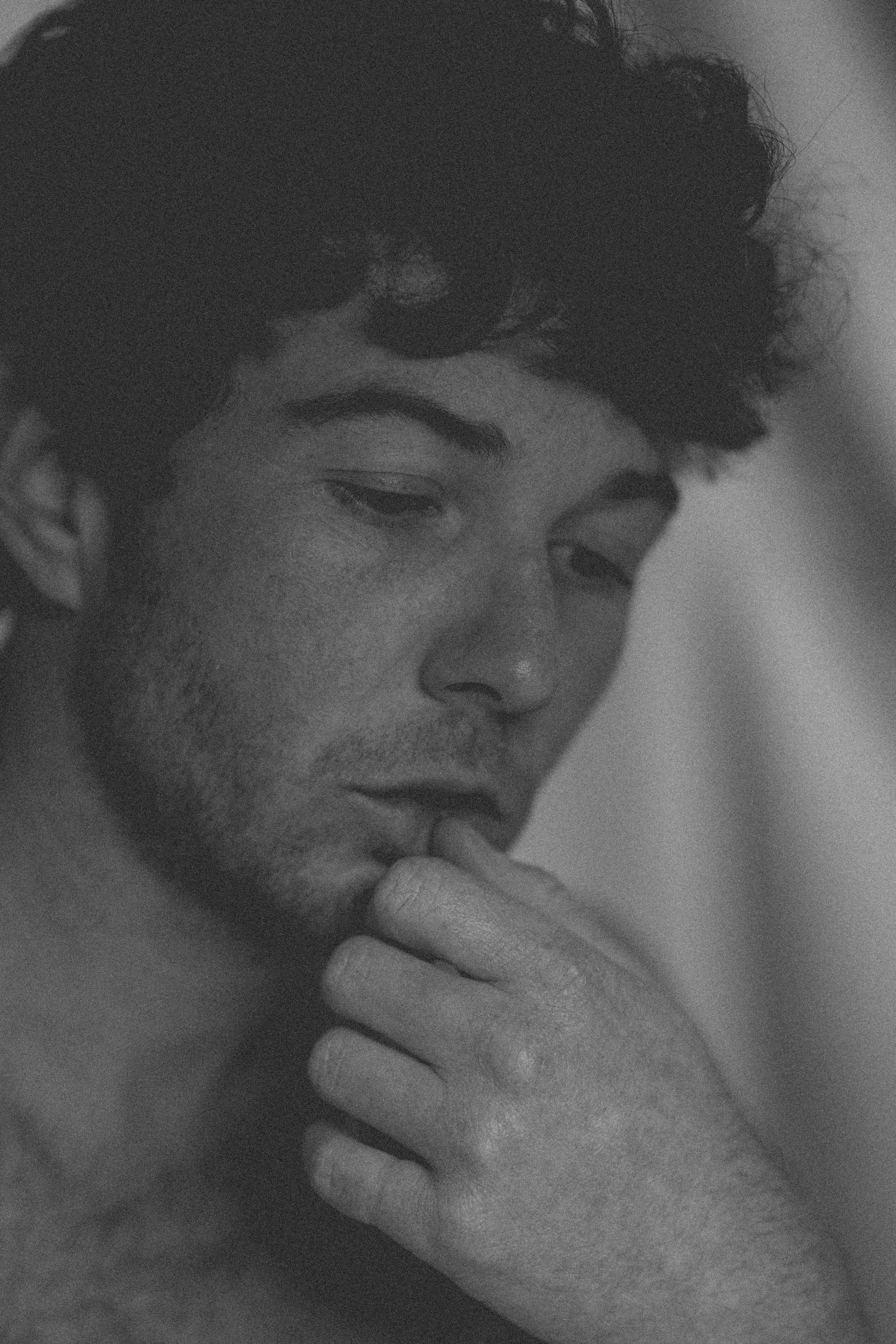 Black and white portrait of thoughtful young man with curly hair resting hand on chin.