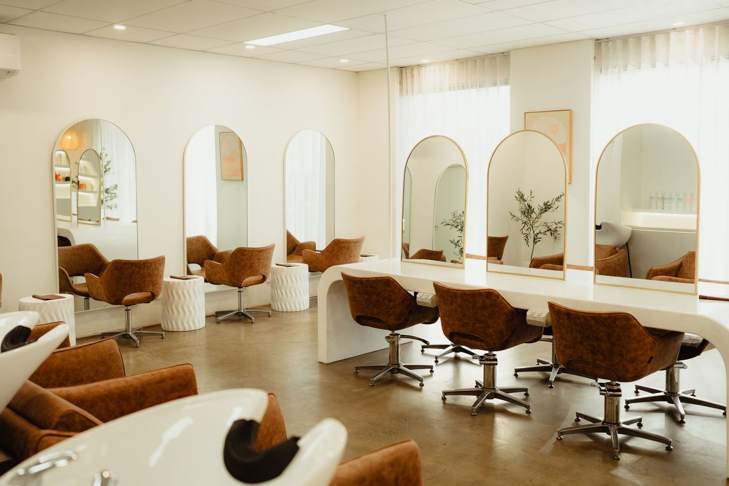 Modern hair salon interior with arched mirrors, brown velvet chairs, and white curved styling stations.