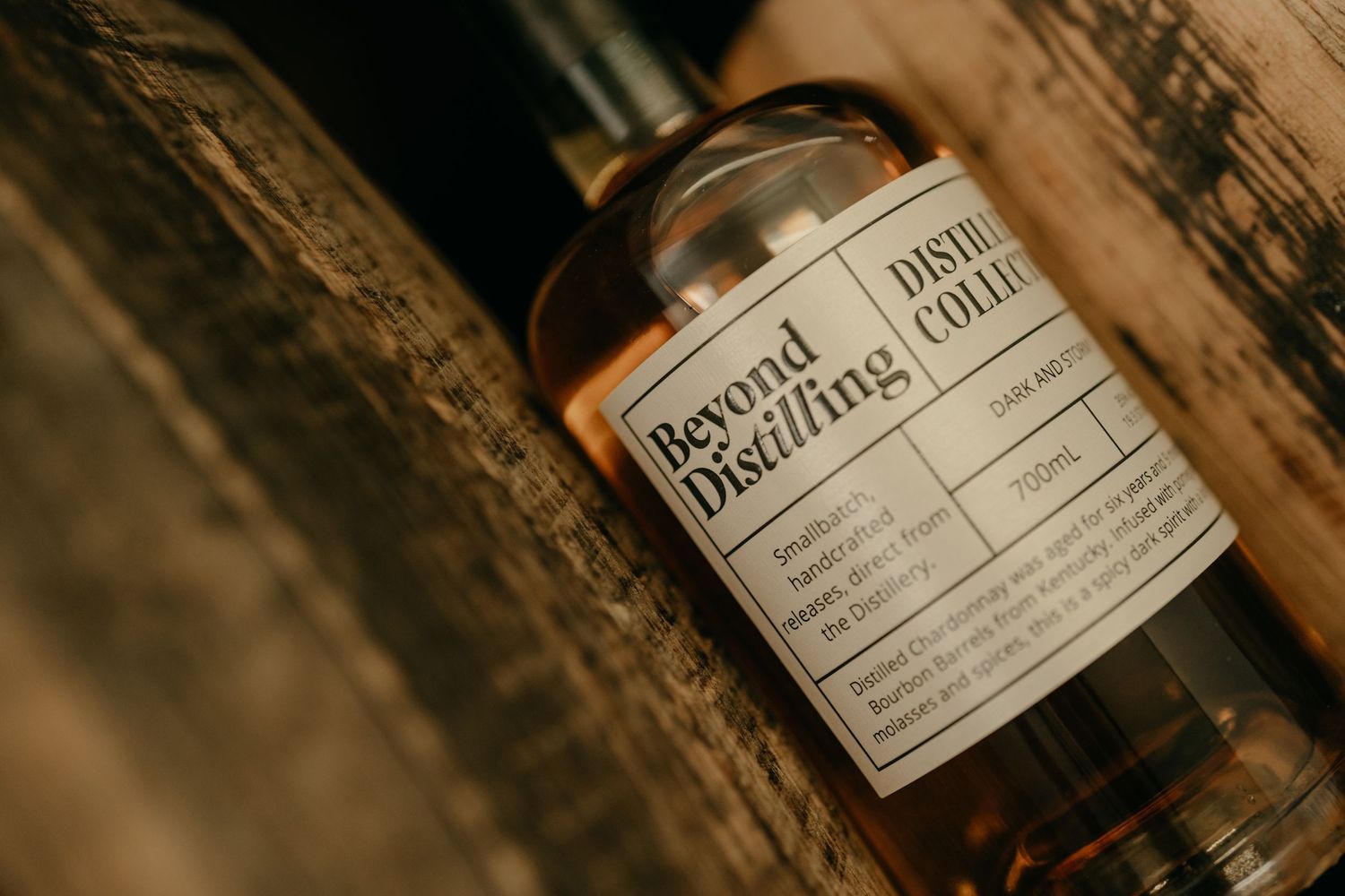 Close-up of a Beyond Distilling spirits bottle resting against a rustic wooden barrel.