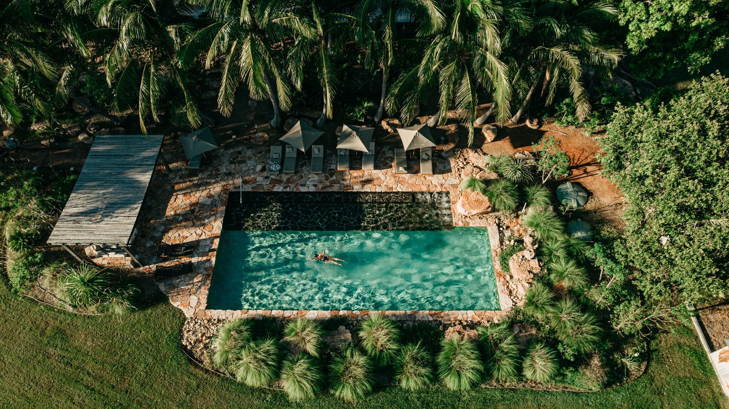 Aerial view of rectangular swimming pool surrounded by lush tropical palm trees and gardens.