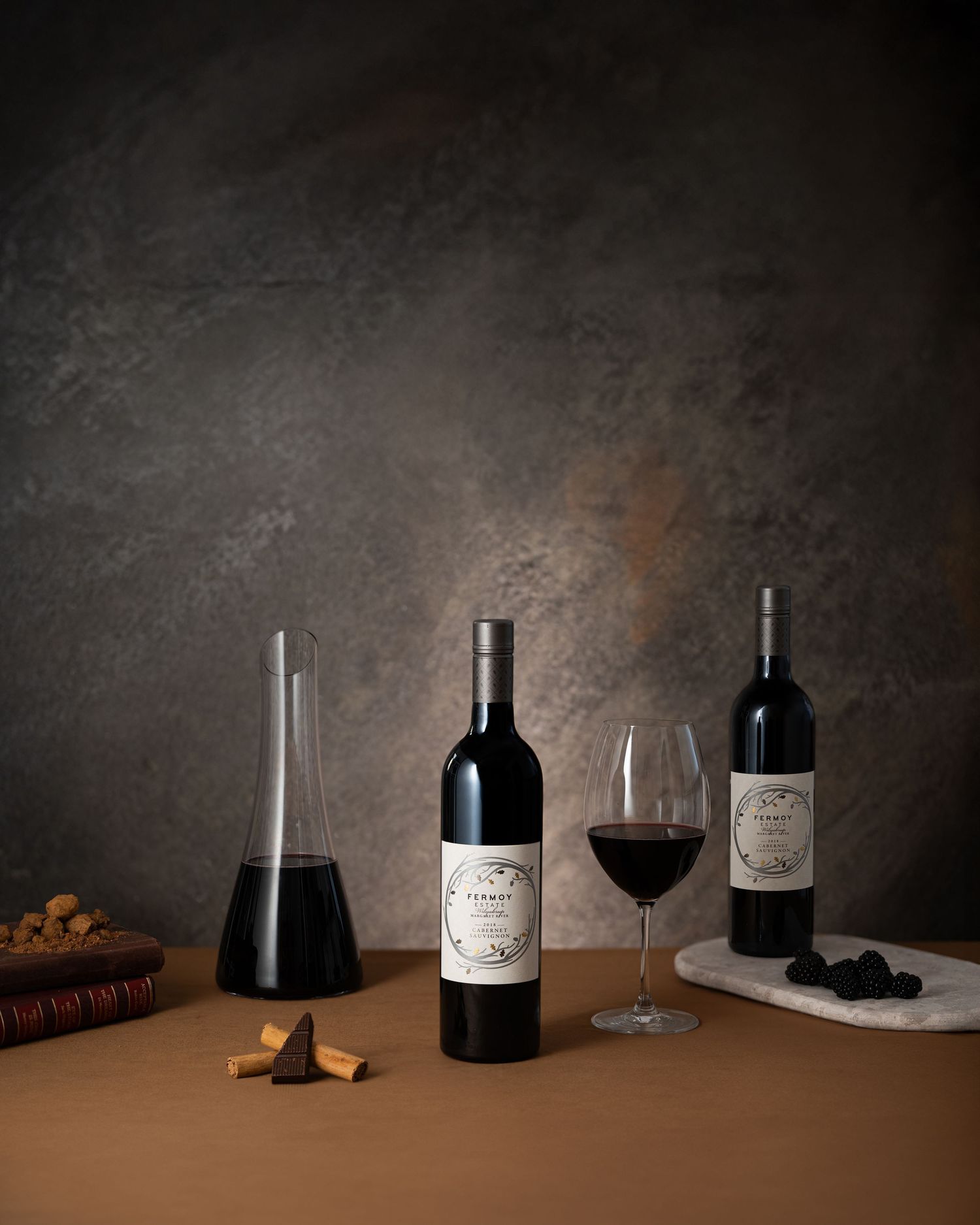 Two red wine bottles, a crystal decanter, and a wine glass arranged on a table with corks and truffles.