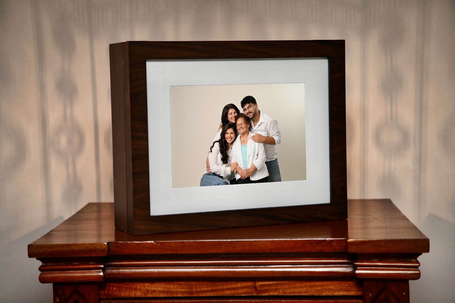 Dark wood framed family portrait photo displayed on a wooden dresser against a neutral wallpaper background.