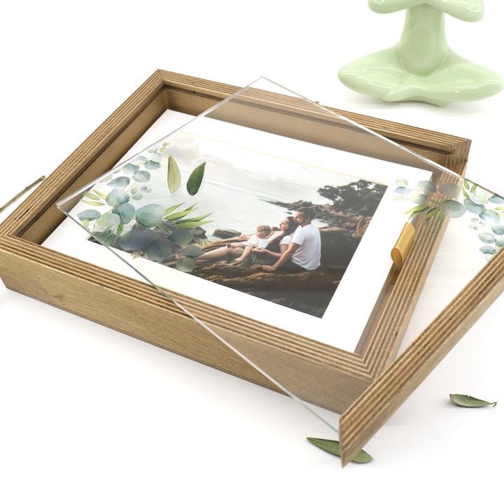Rustic wooden shadow box frame with family photo and eucalyptus leaves on a light surface.