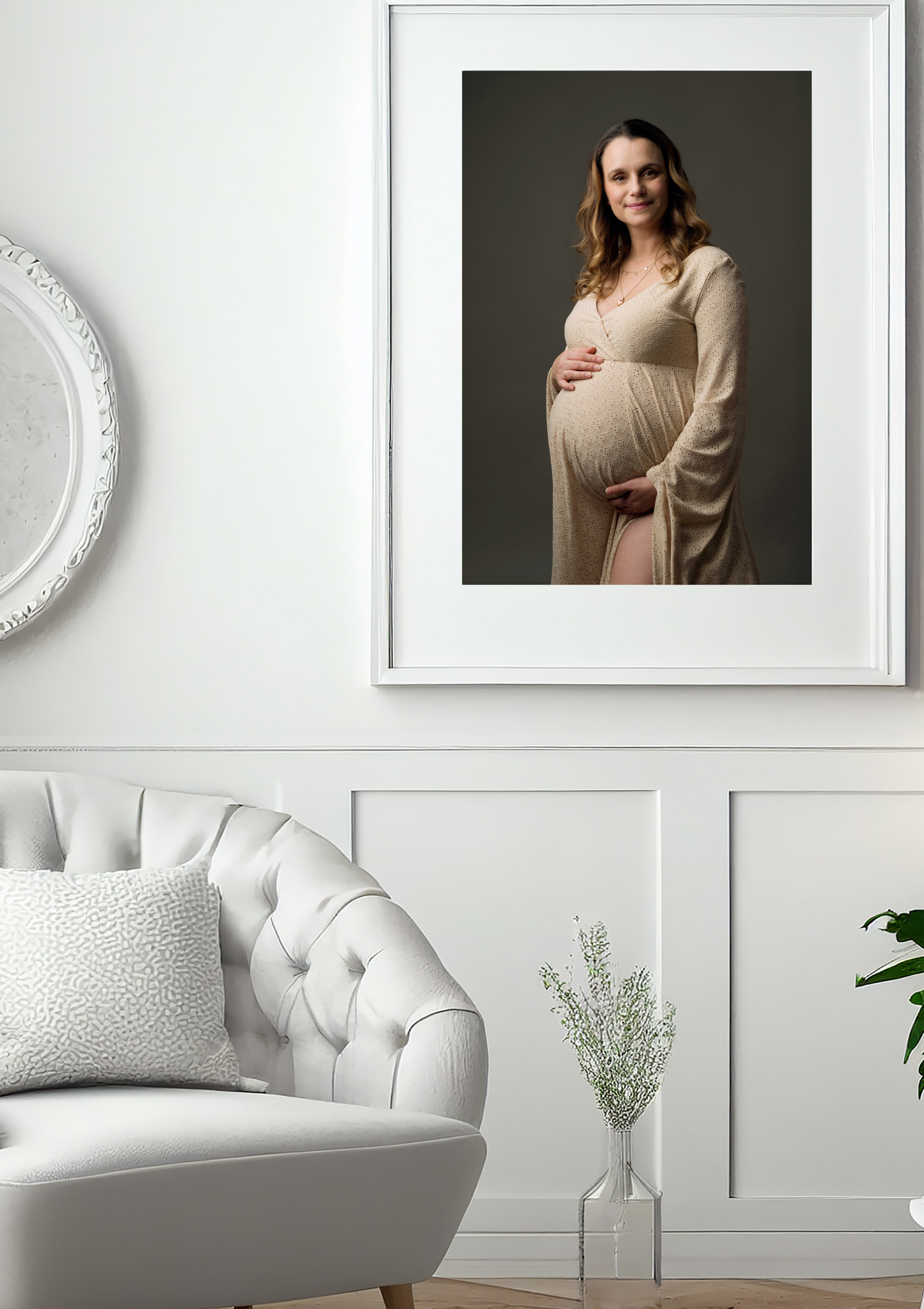 Framed maternity portrait of a woman in a beige dress displayed in a white elegant living room.