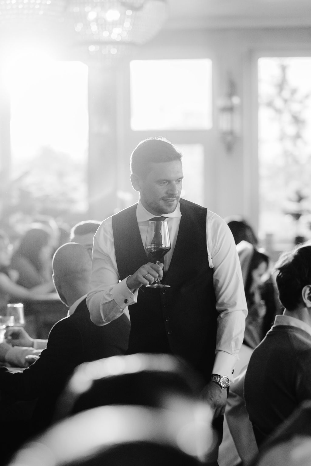 Black and white photo of a wedding reception with guests toasting and mingling in an elegant indoor setting.