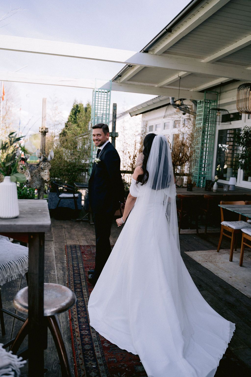 A couple celebrates their wedding day on an outdoor terrace decorated with white accents and greenery.
